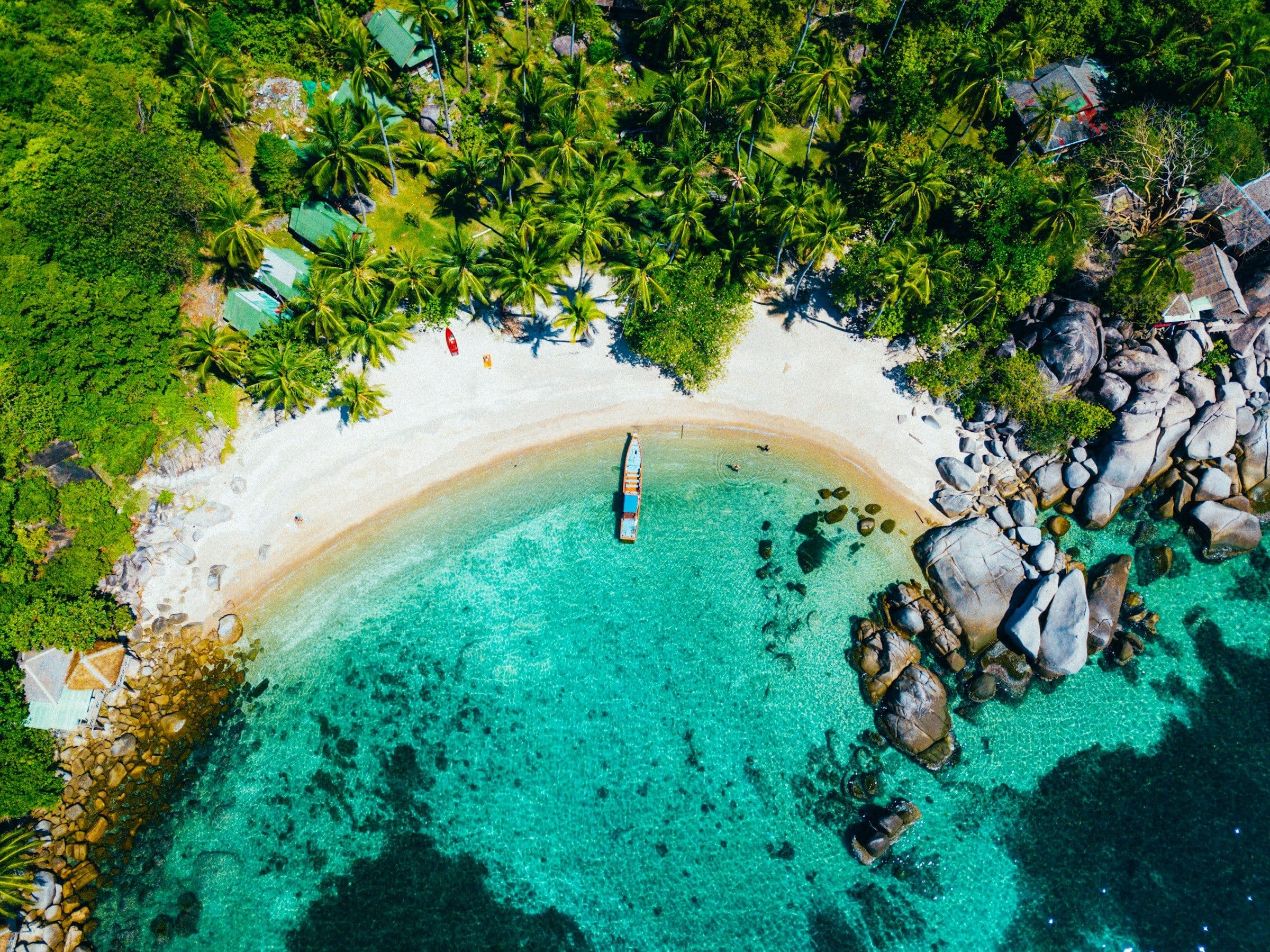 A small curved beach, granite boulders and clear turquoise water on the island of Koh Tao, Thailand, seen from the air.