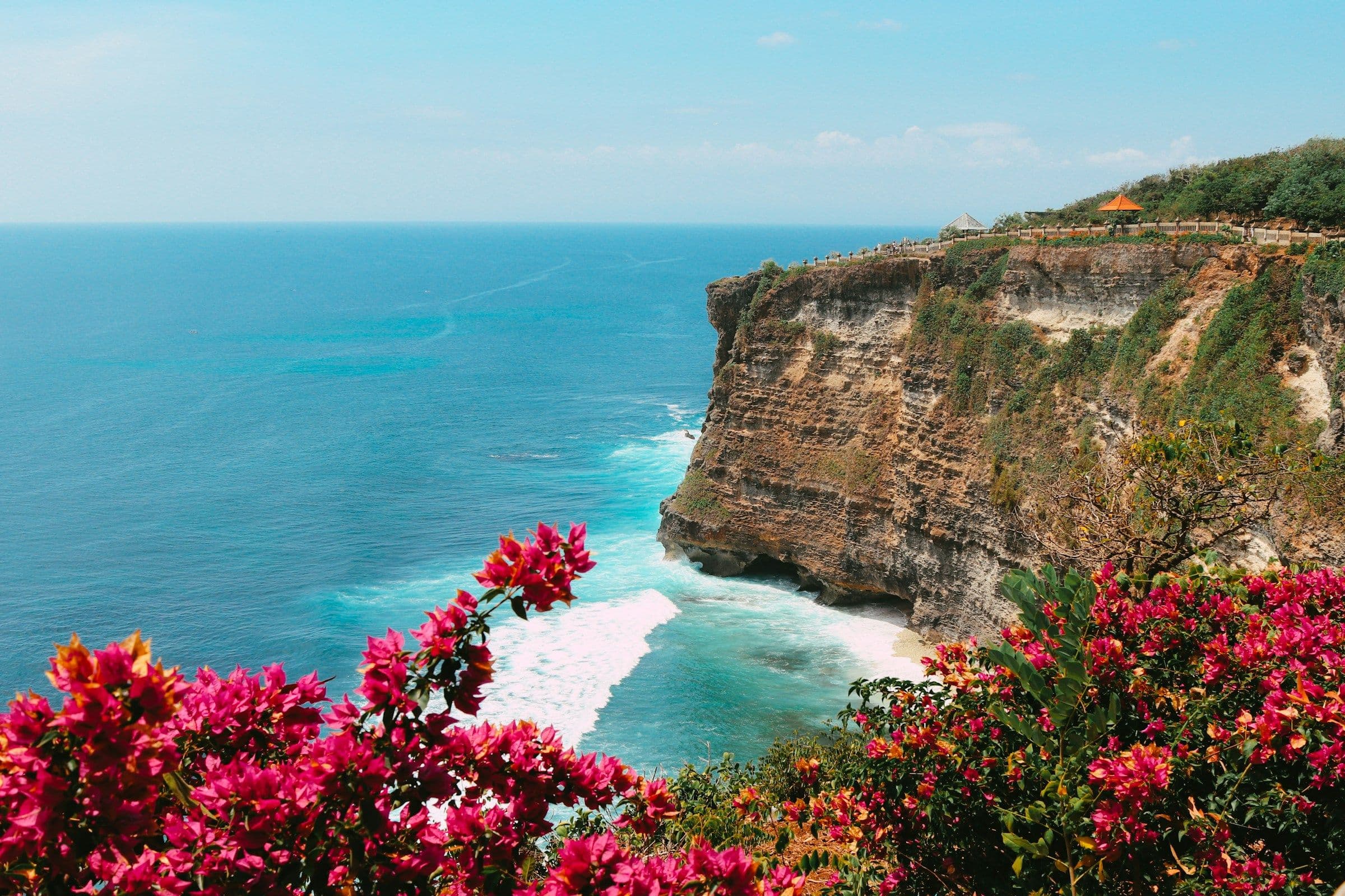 High limestone cliffs above a turquoise sea at Uluwatu, Bali, with bougainvillea in the foreground.