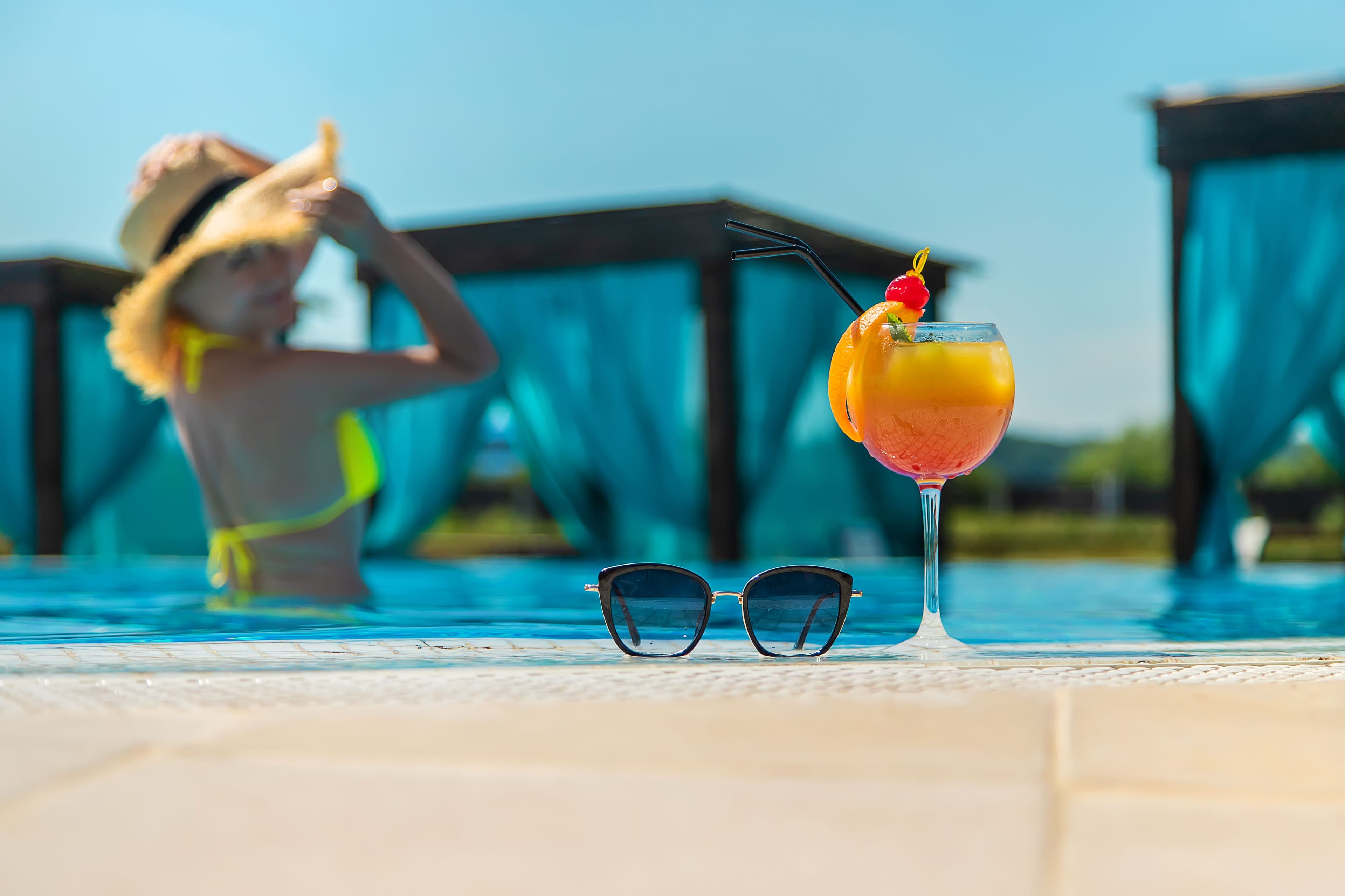 woman at pool with cocktail and sunglasses