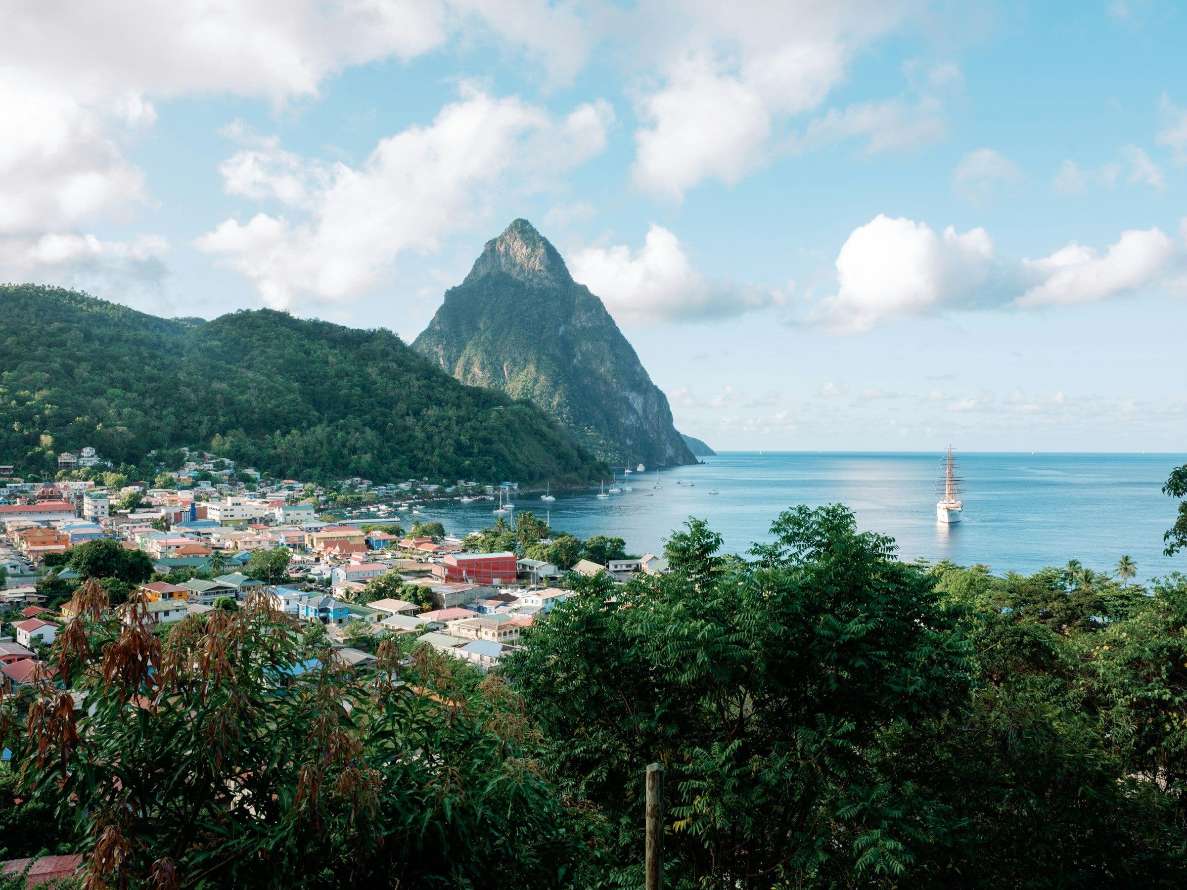 The harbour town of Soufrière below the Petit Piton in St Lucia, with a sailing ship in the bay.