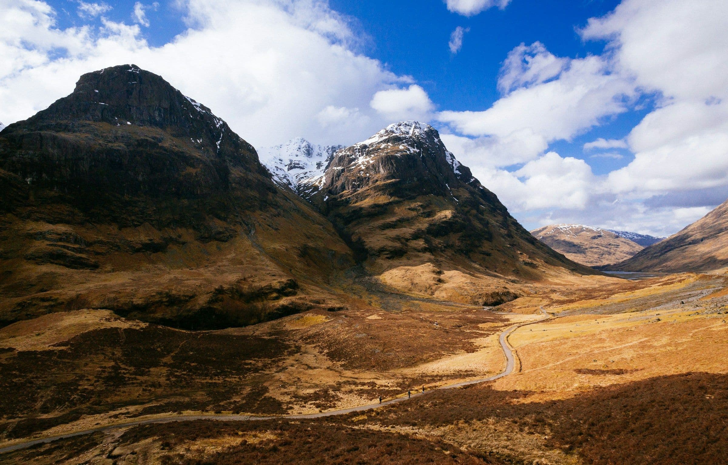 The mountains of Glencoe in the Scottish Highlands under a bright, cloudy sky.