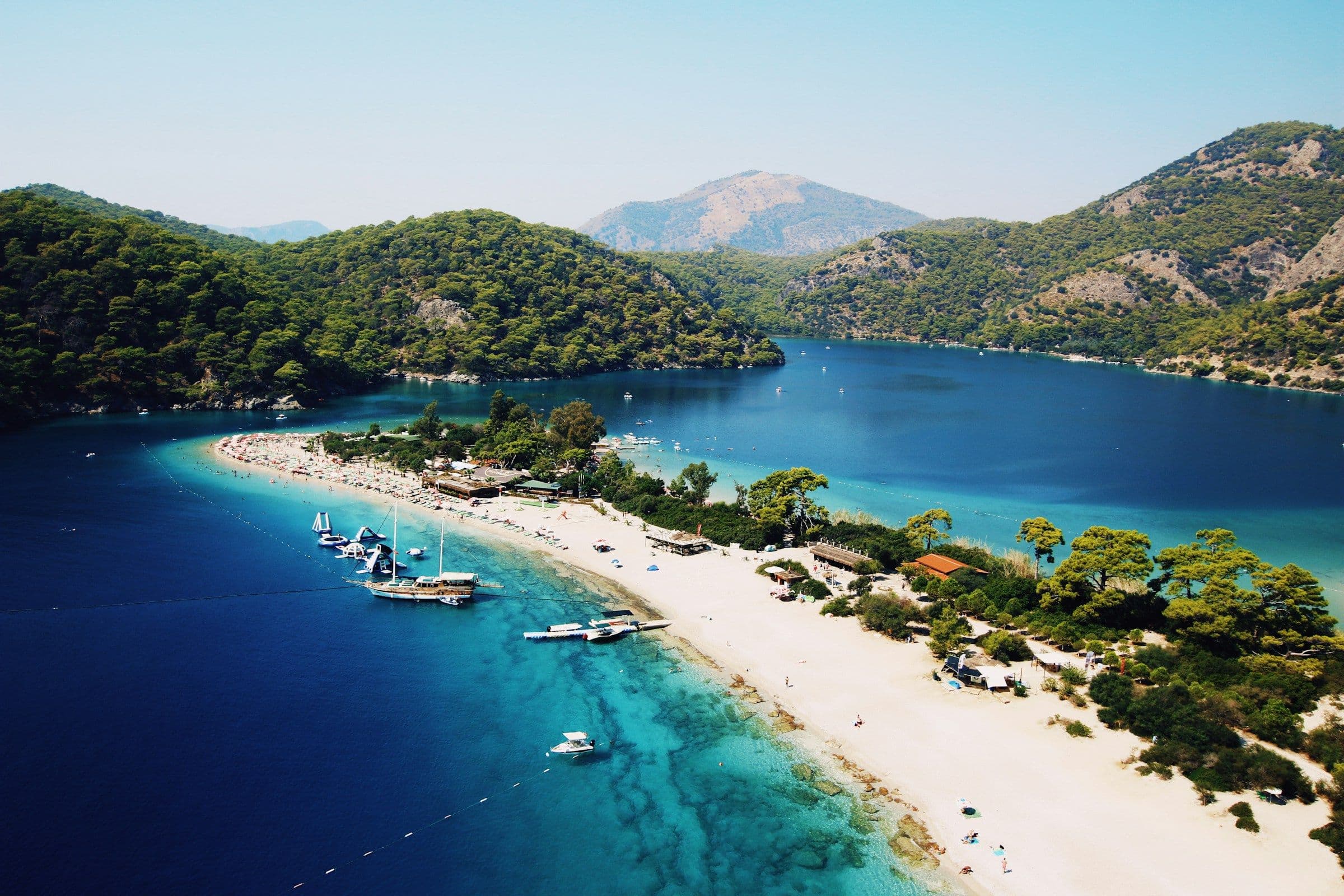 The beach and sheltered blue lagoon at Ölüdeniz on the Turkish coast, backed by pine-covered hills, seen from the air.