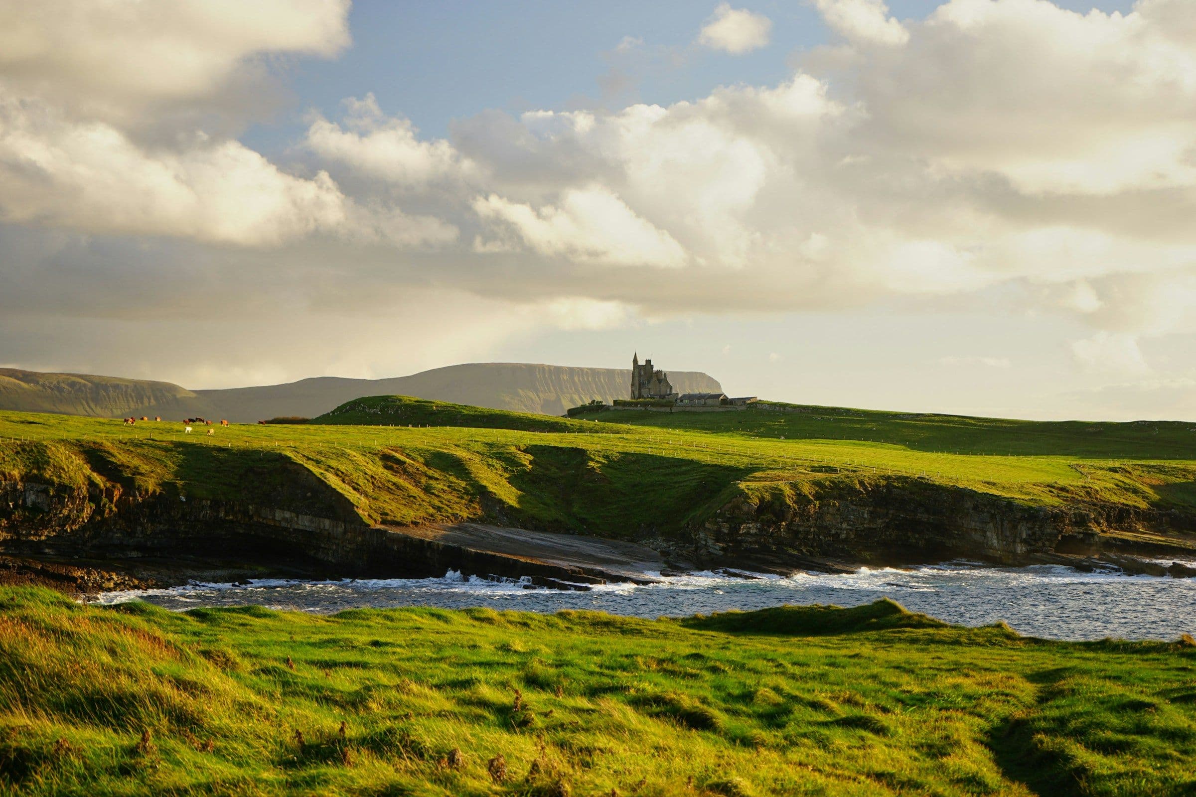 A ruined castle on a green headland above the sea in County Donegal, Ireland.