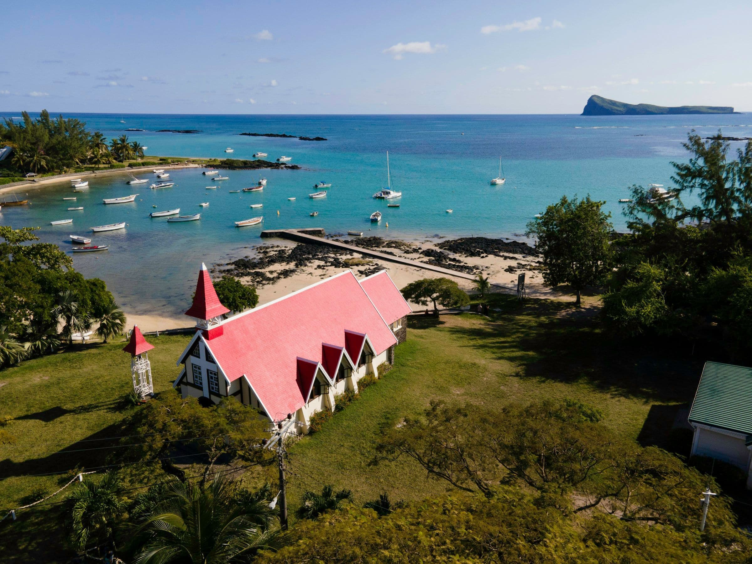 The red-roofed church at Cap Malheureux on the north coast of Mauritius, beside a bay of small boats, seen from the air.