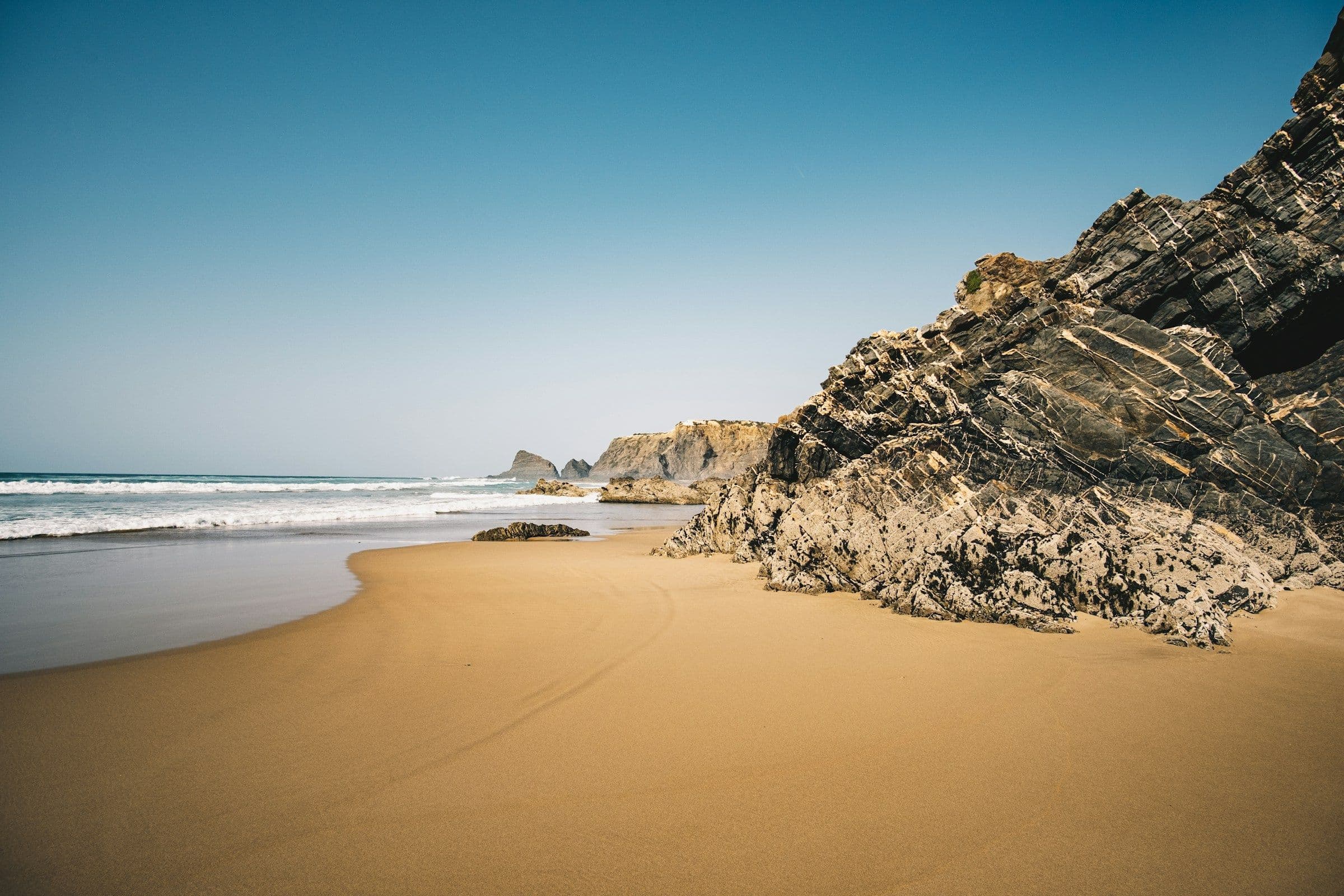 An empty golden beach below layered rock cliffs on the coast of the Algarve, Portugal.