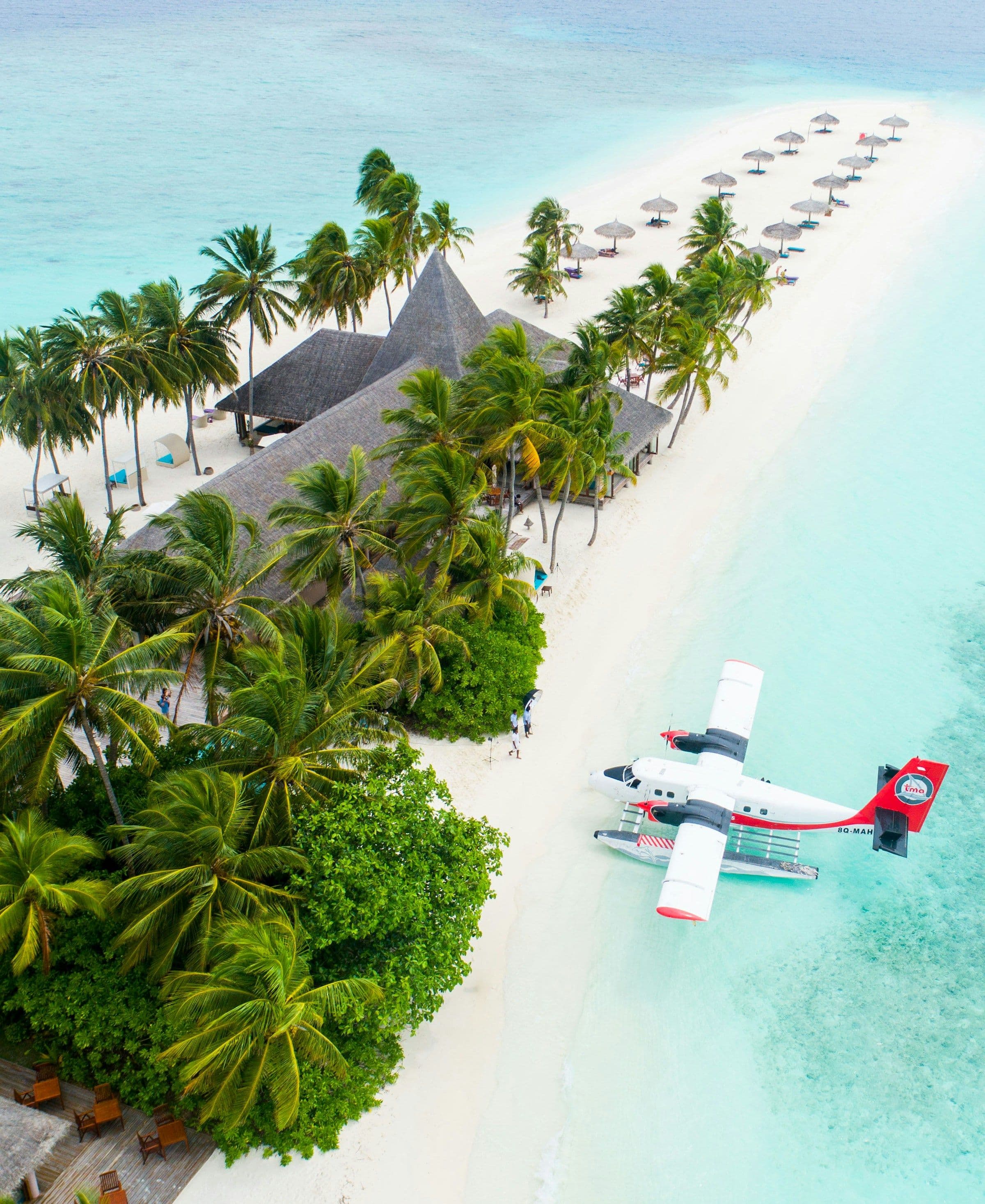 A seaplane moored beside a palm-covered island and white sandbank in the Maldives, seen from the air.