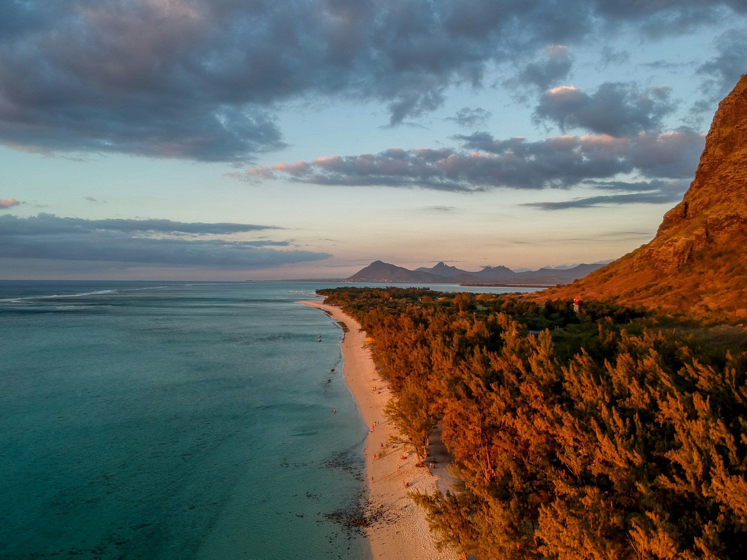 The beach at Le Morne in Mauritius in evening light, with trees along the shore and the mountain rising behind.