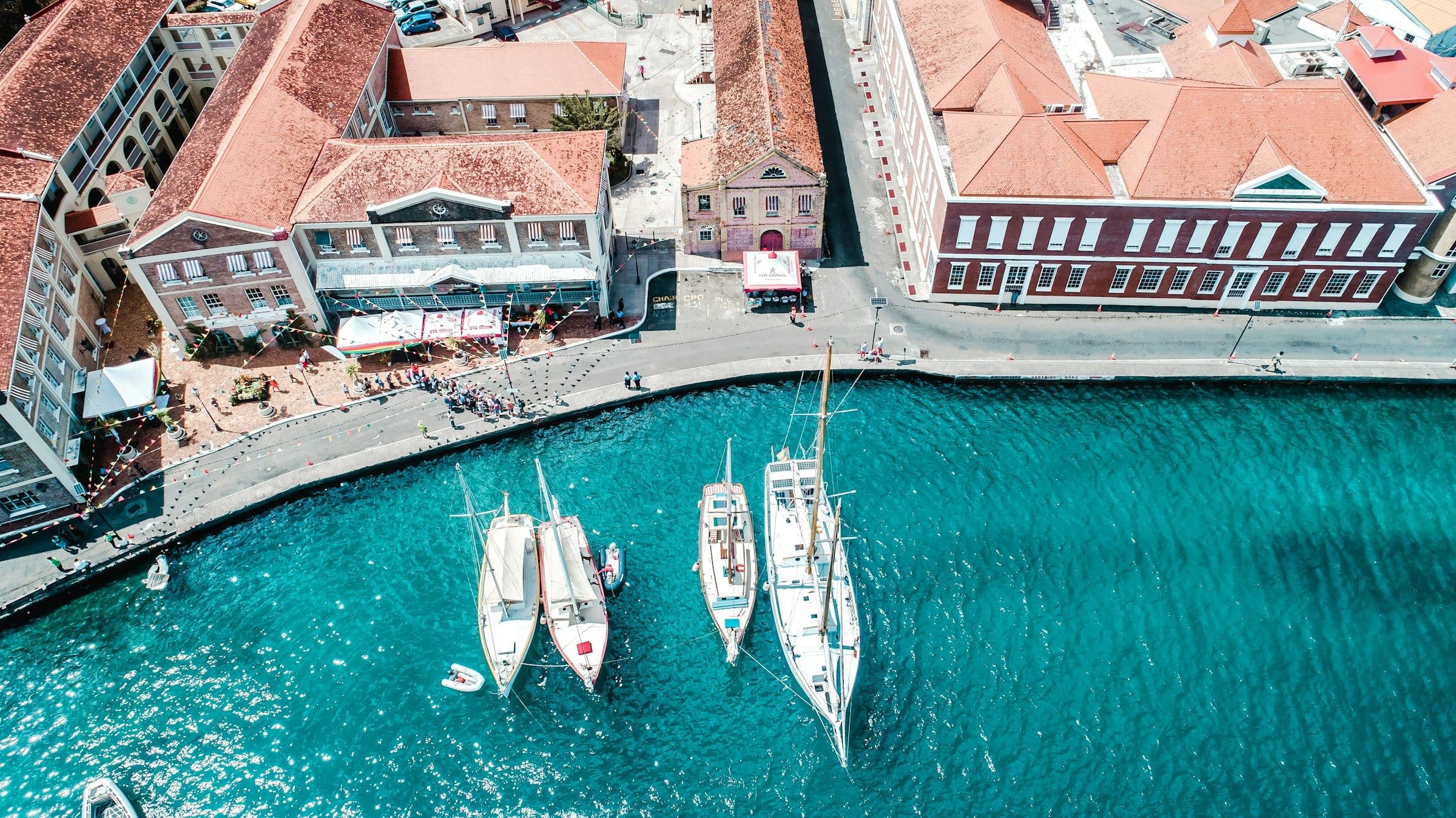 Sailing boats moored at the waterfront of St George’s, Grenada, below red-roofed Georgian buildings, seen from the air.