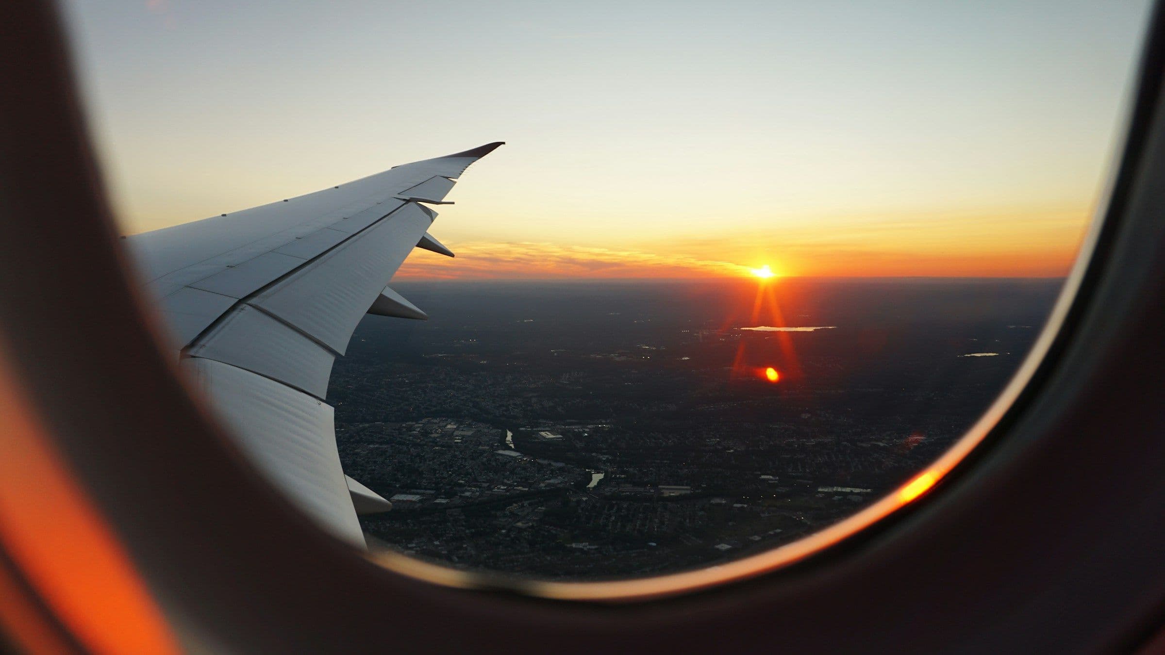 An aircraft wing seen through a cabin window at sunset.