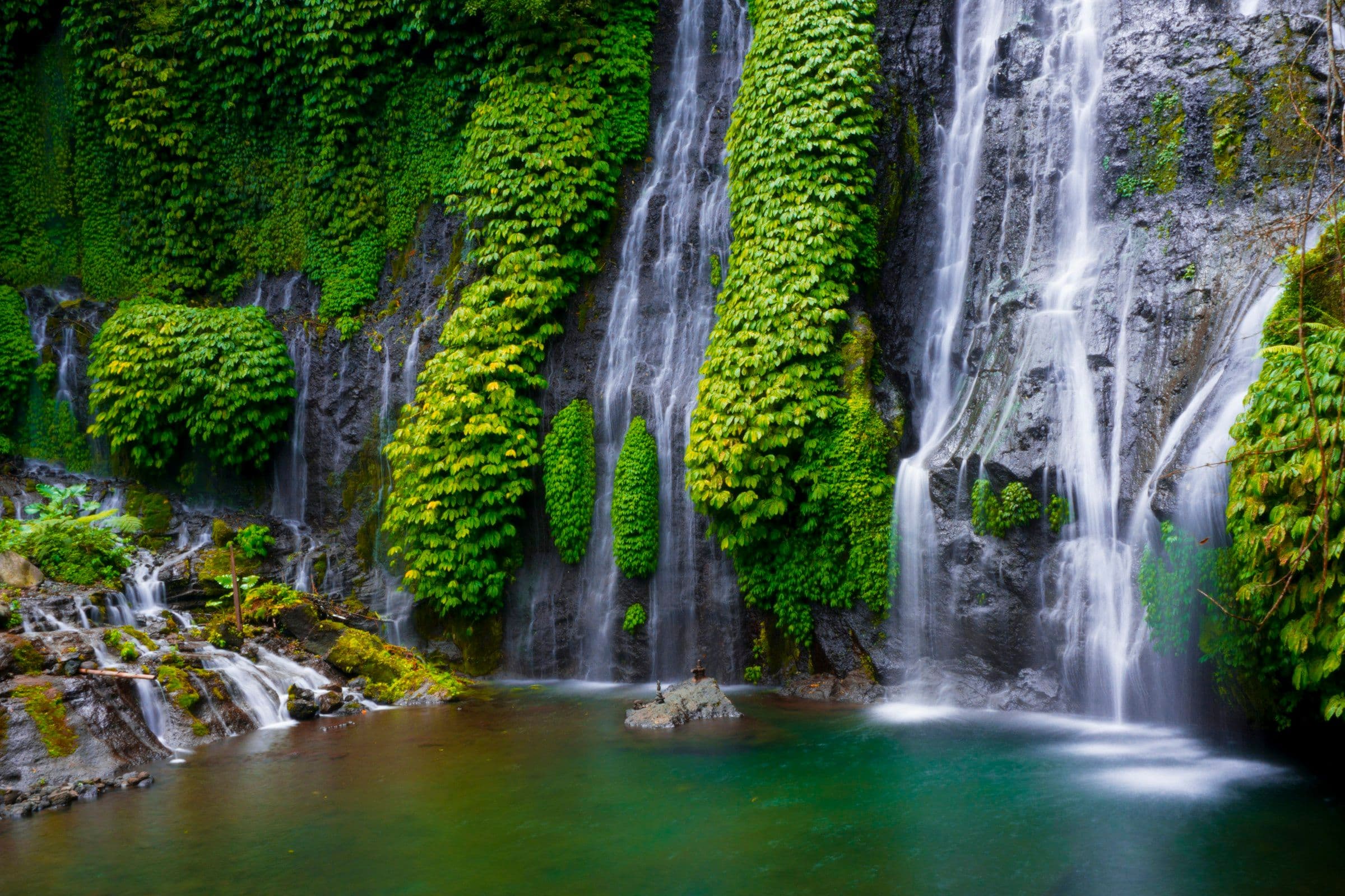 The Banyumala waterfall in the north of Bali, falling in several streams over a mossy rock face into a pool.