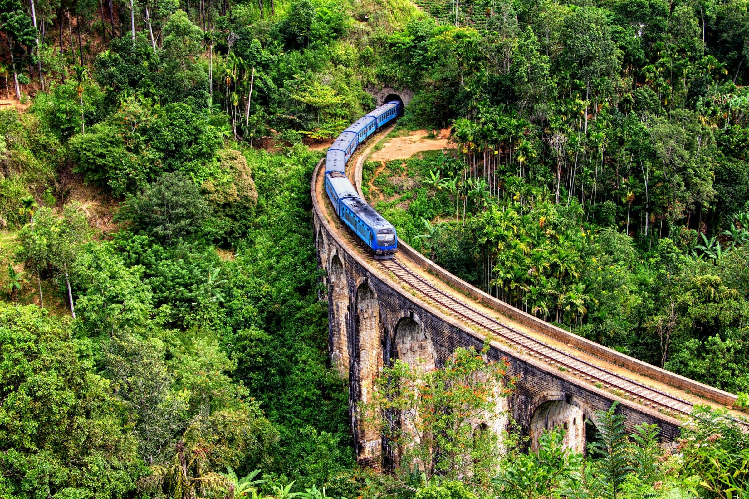 A blue train crossing the stone Nine Arch Bridge among forest near Ella, Sri Lanka.