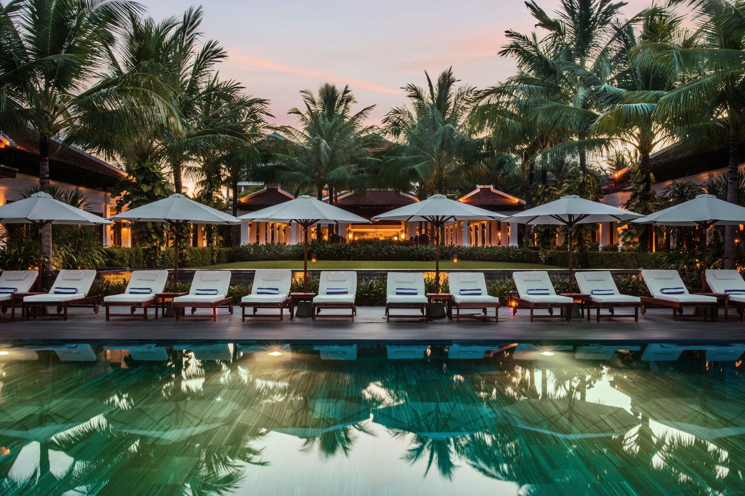 Sun loungers and red parasols beside a palm-lined pool at a resort in Vietnam.