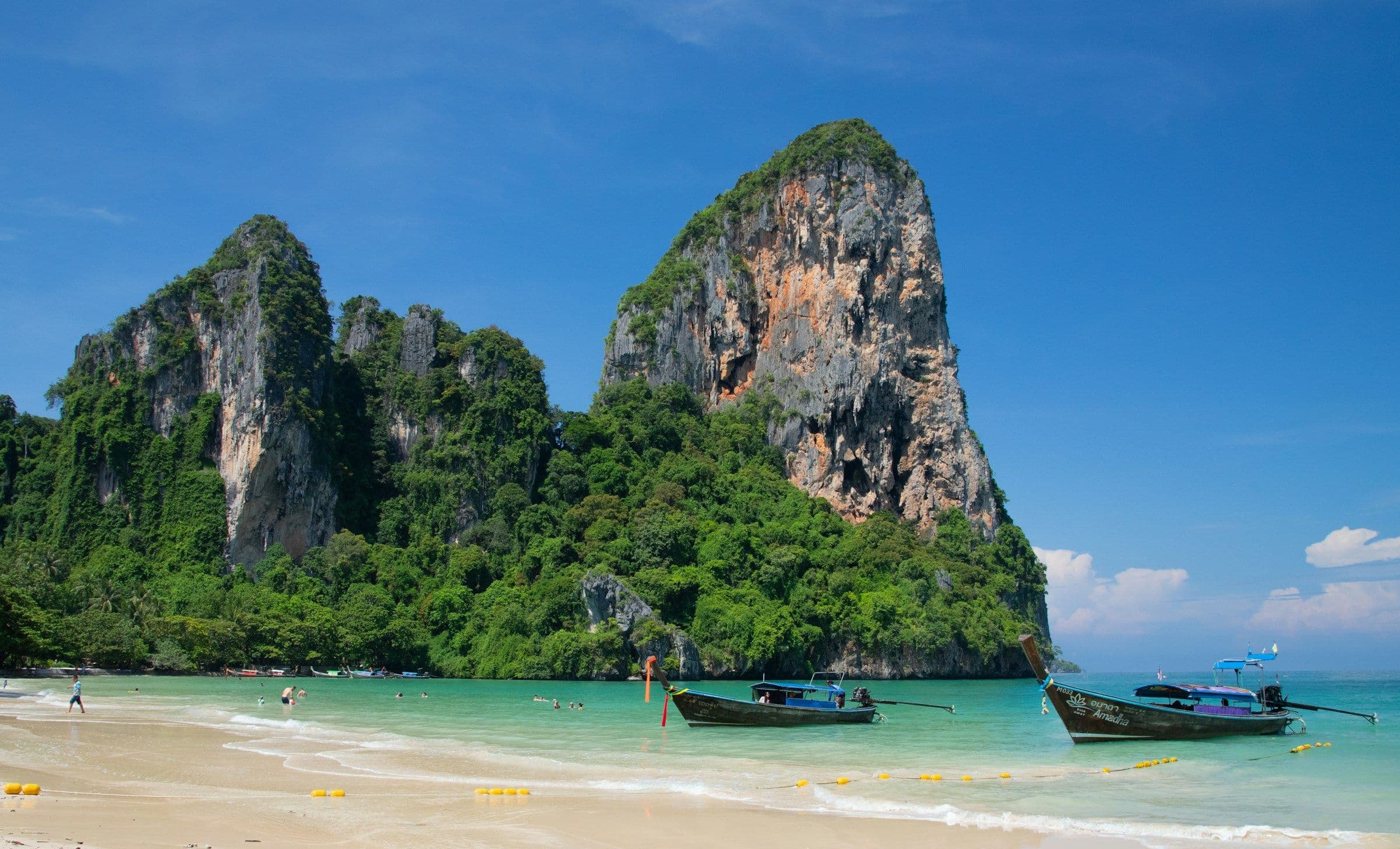 Longtail boats on the sand at Railay Beach, Thailand, beneath limestone cliffs covered in forest.