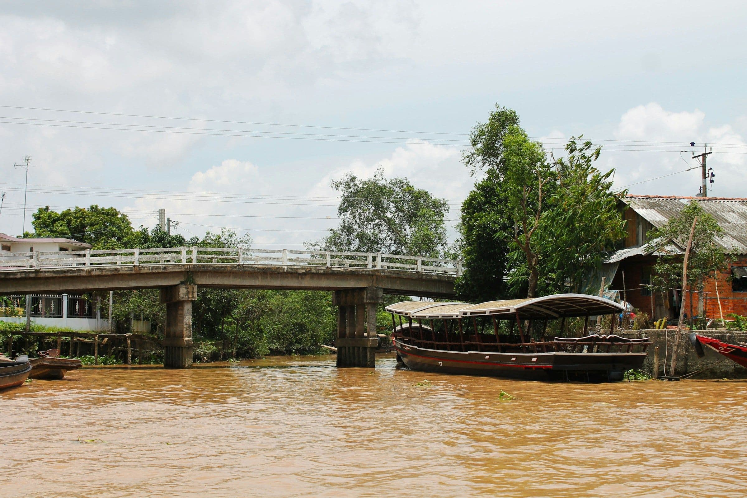 A wooden boat moored beside a bridge on a brown river in the Mekong Delta, Vietnam.