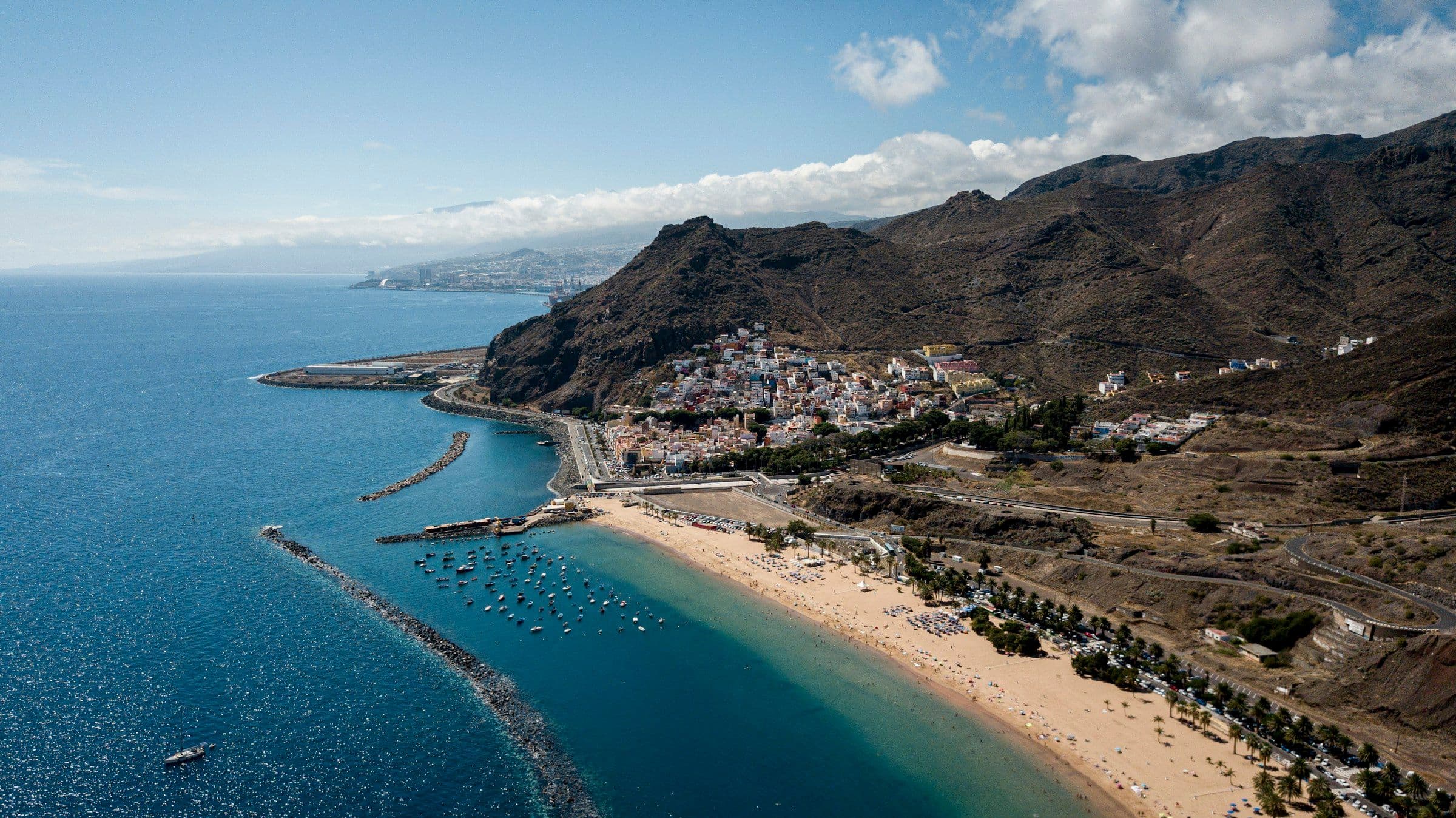 A long golden beach, a village and steep volcanic hills at San Andrés in Tenerife, Canary Islands, seen from the air.