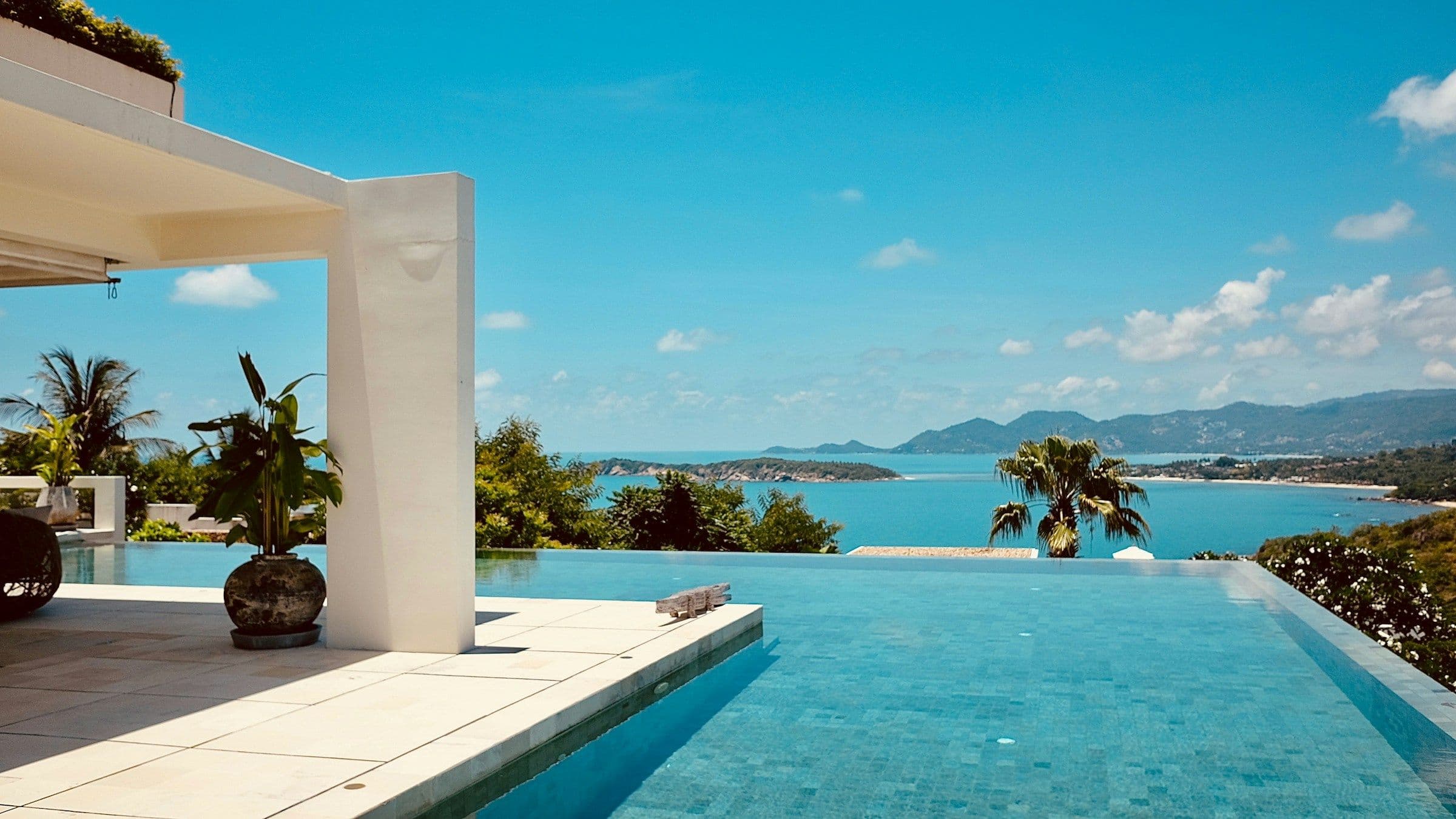 An infinity pool on a villa terrace overlooking a blue bay and distant islands in Koh Samui, Thailand.