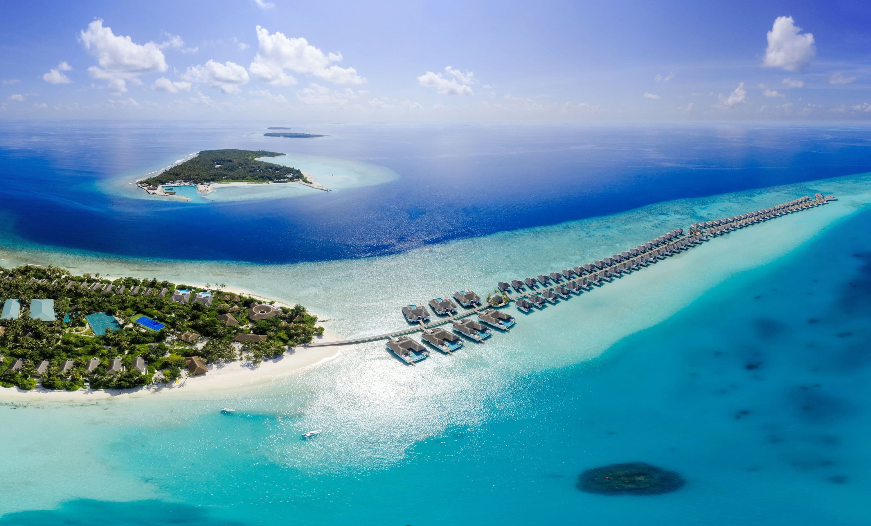 Overwater villas and sandbanks in a turquoise lagoon in the Maldives, seen from the air.