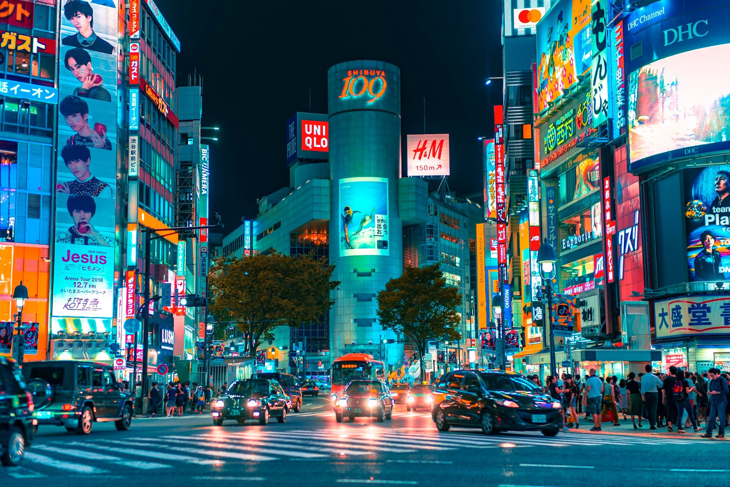 Traffic and neon signs at a busy junction in Shibuya, Tokyo, at night.
