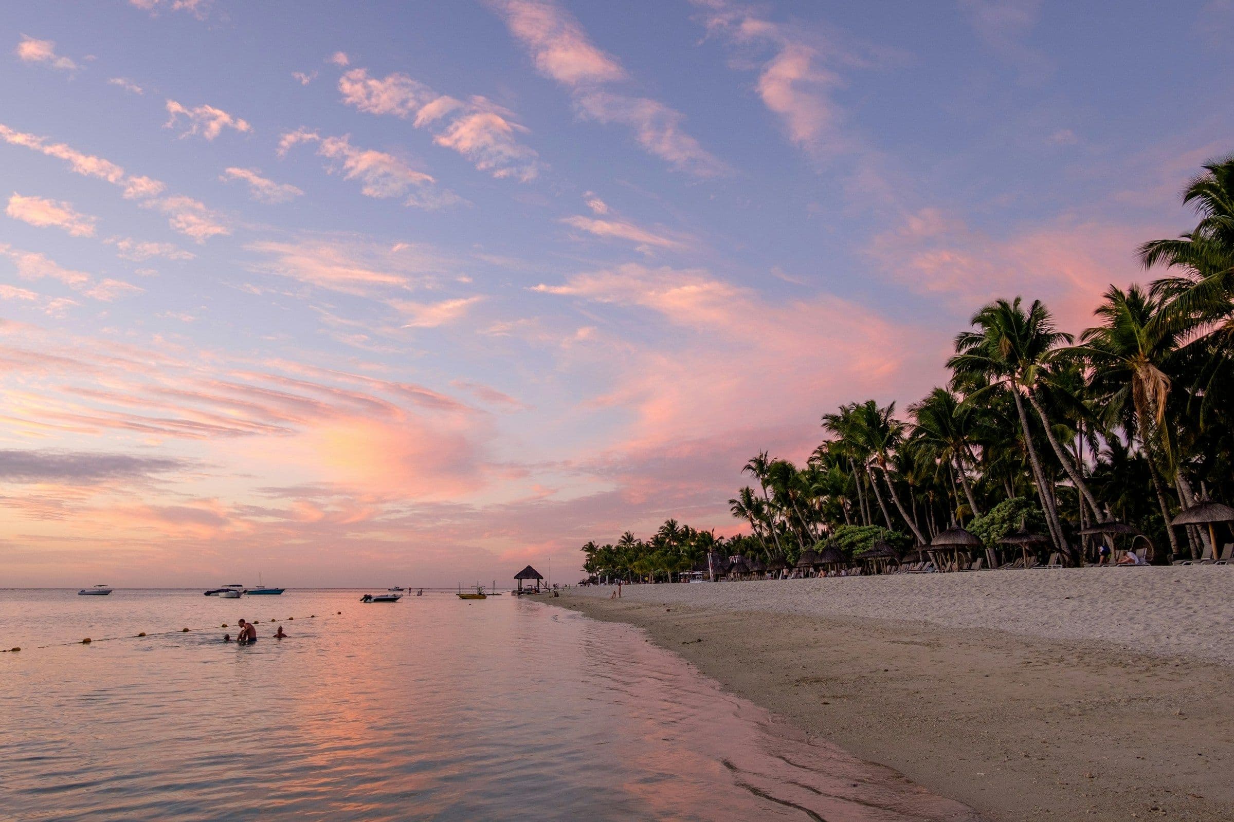 A pink sunset over calm water and a palm-lined beach at Flic en Flac on the west coast of Mauritius.
