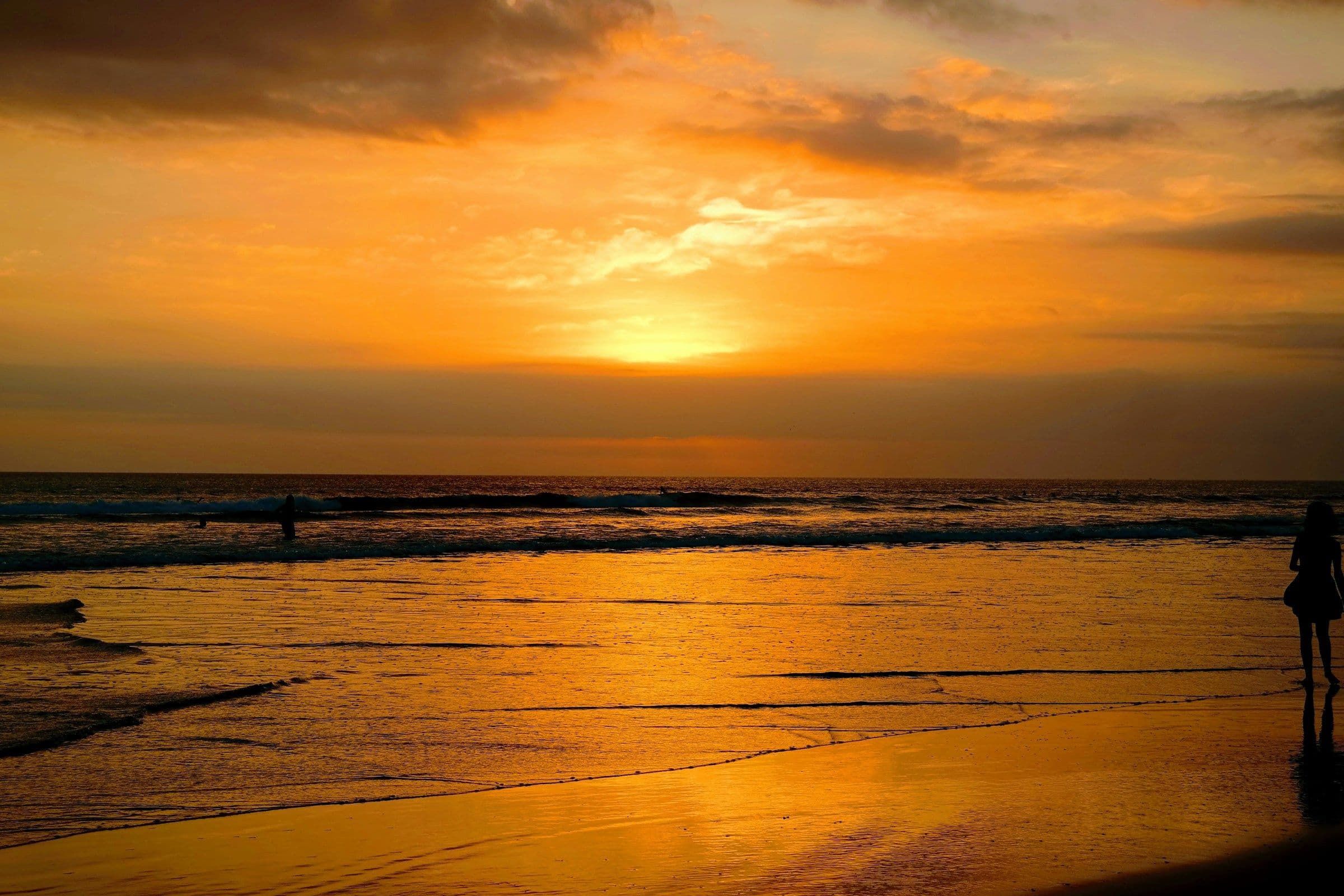 An orange sunset over the sea and wet sand at Seminyak, Bali.