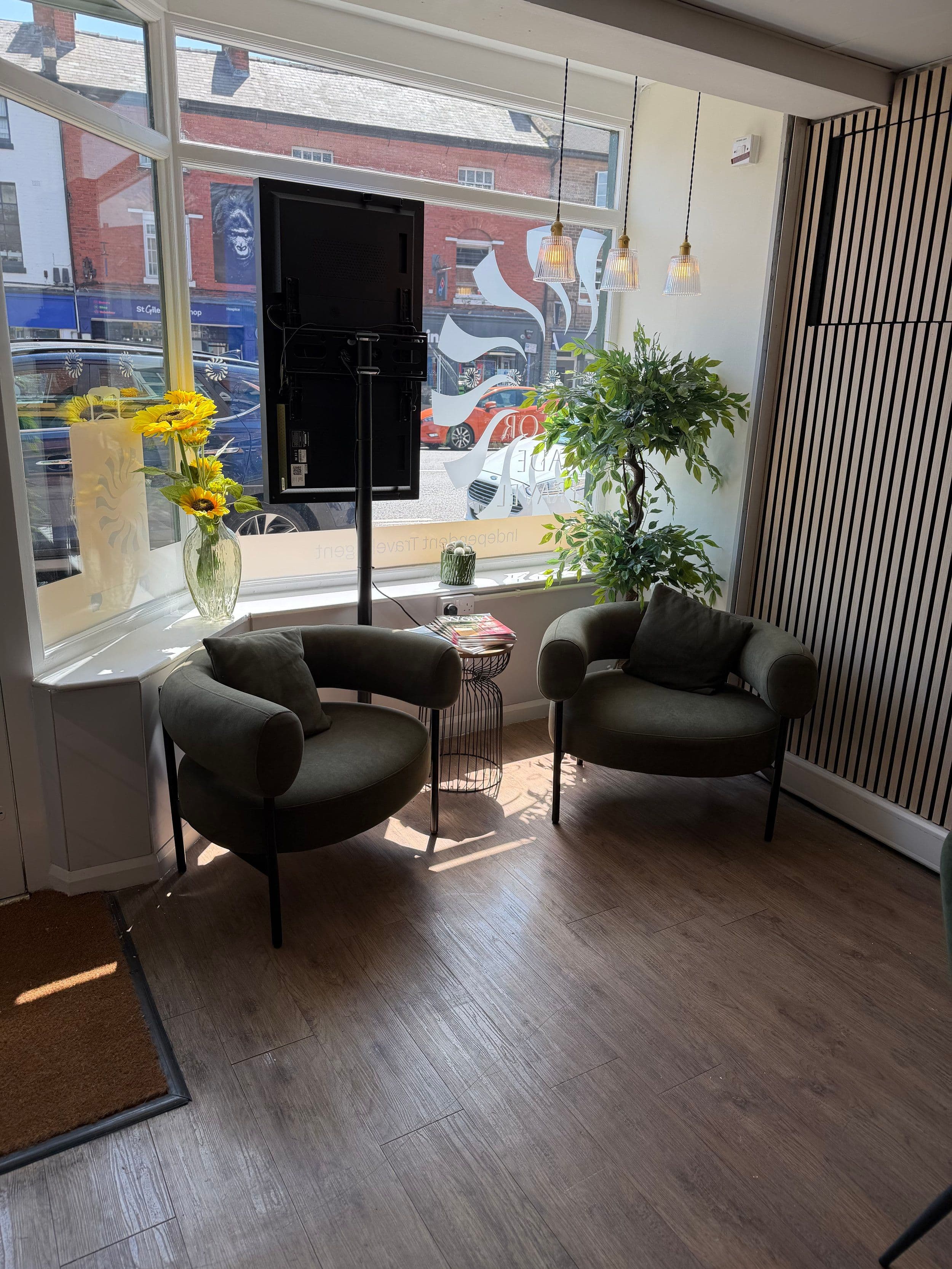 The seating area of the Auria Travel store: two green armchairs and a plant by the front window.