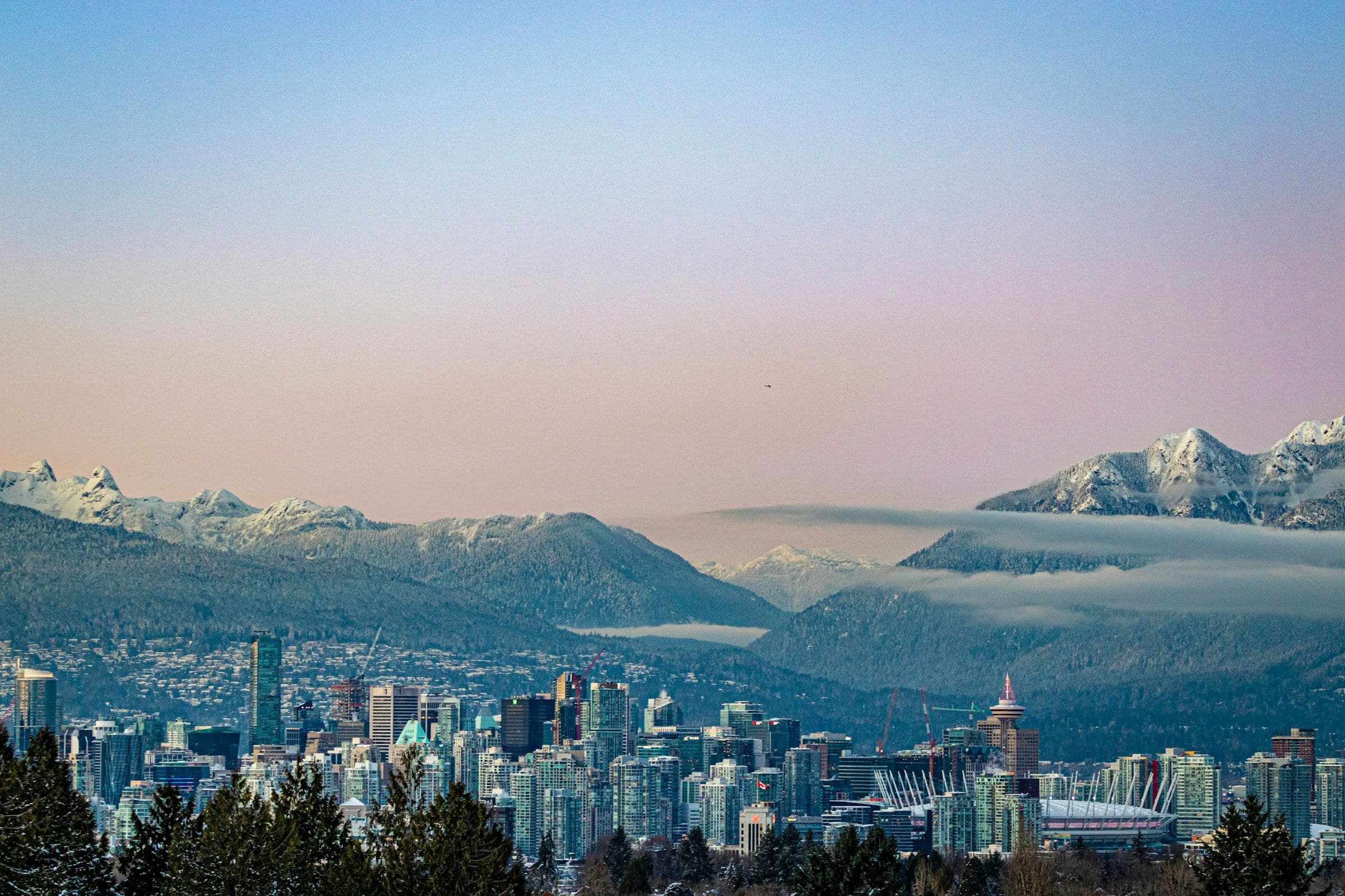 The towers of Vancouver, Canada, beneath snow-covered mountains at sunset.