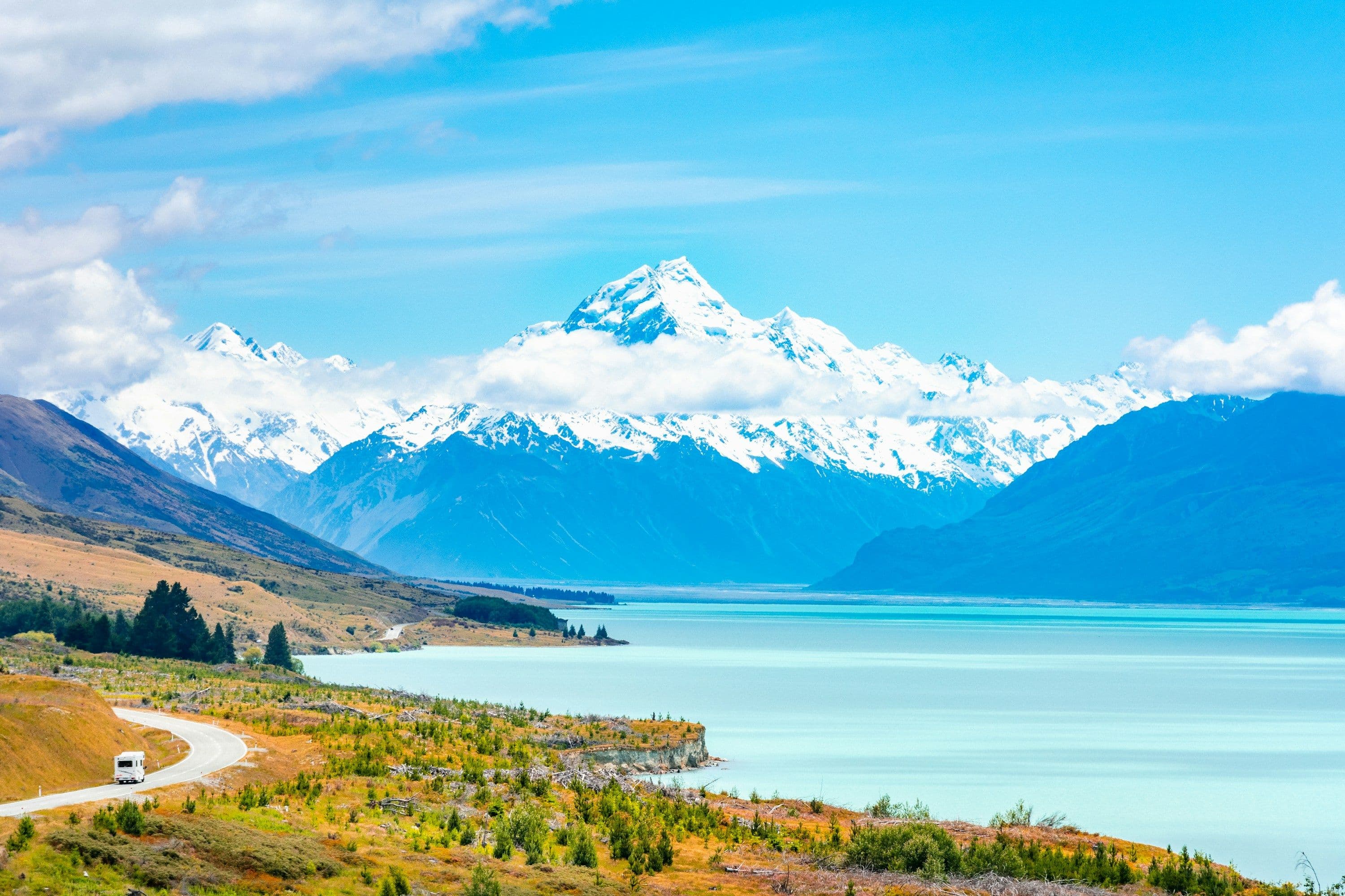 A campervan on the road beside turquoise Lake Pukaki, with snow-covered Aoraki / Mount Cook ahead, New Zealand.