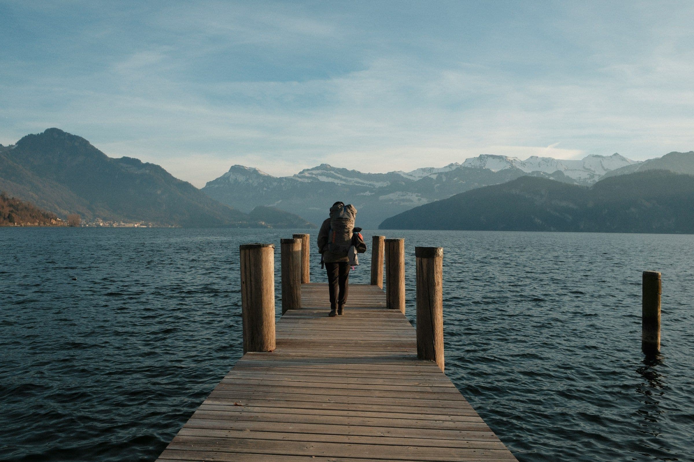 A lone figure at the end of a wooden jetty on Lake Lucerne, Switzerland, facing the mountains.
