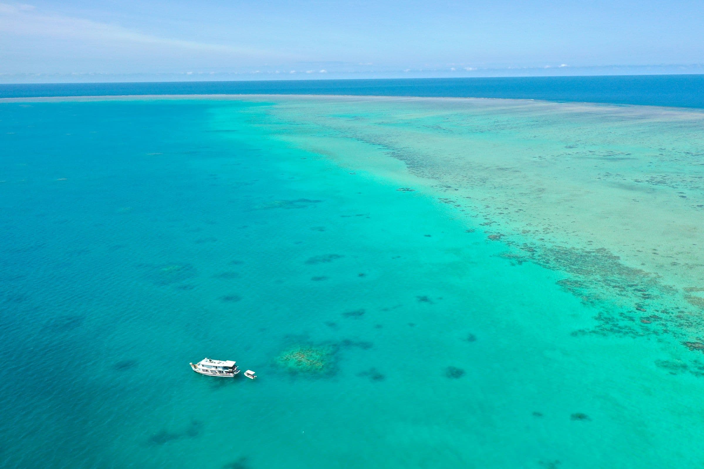 A boat moored in clear turquoise water over the reef at Michaelmas Cay on the Great Barrier Reef, seen from the air.