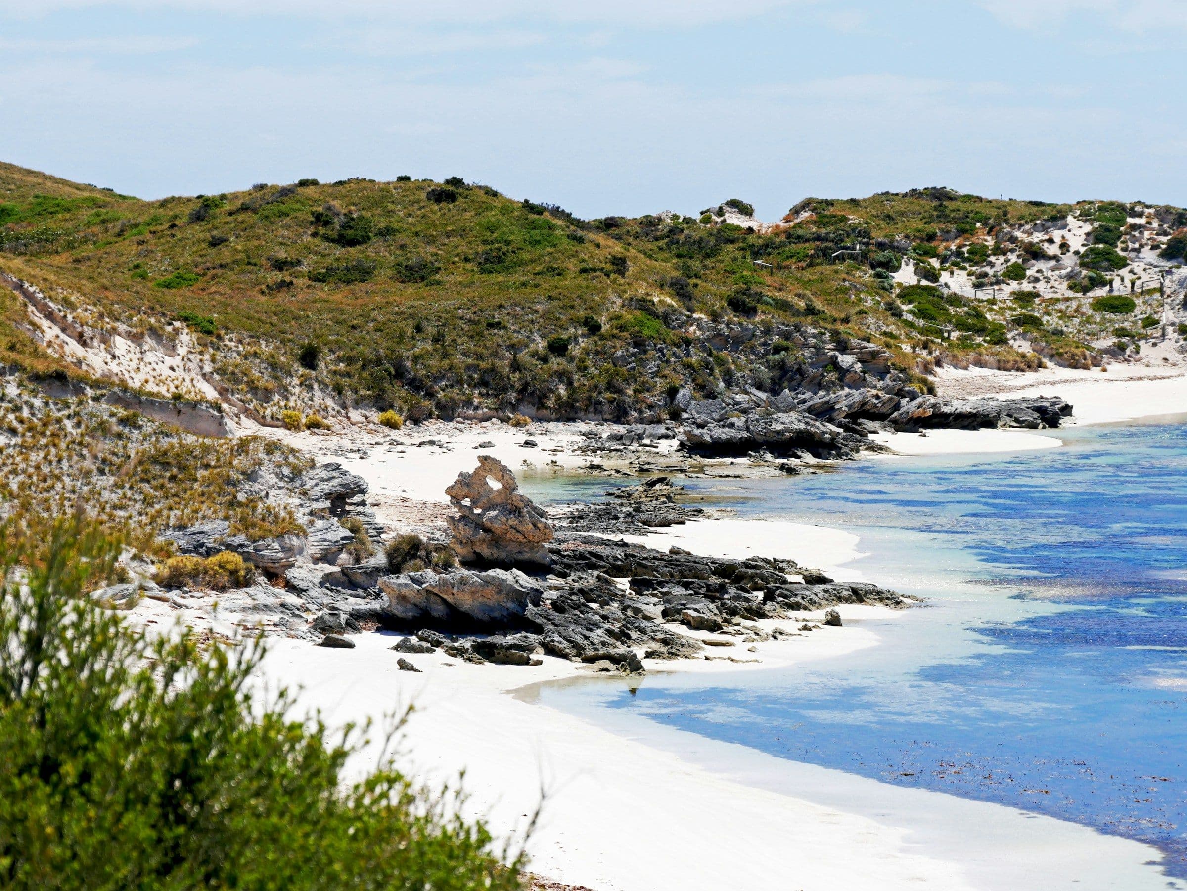White sand, rocks and clear blue water in a bay on Rottnest Island, Western Australia.
