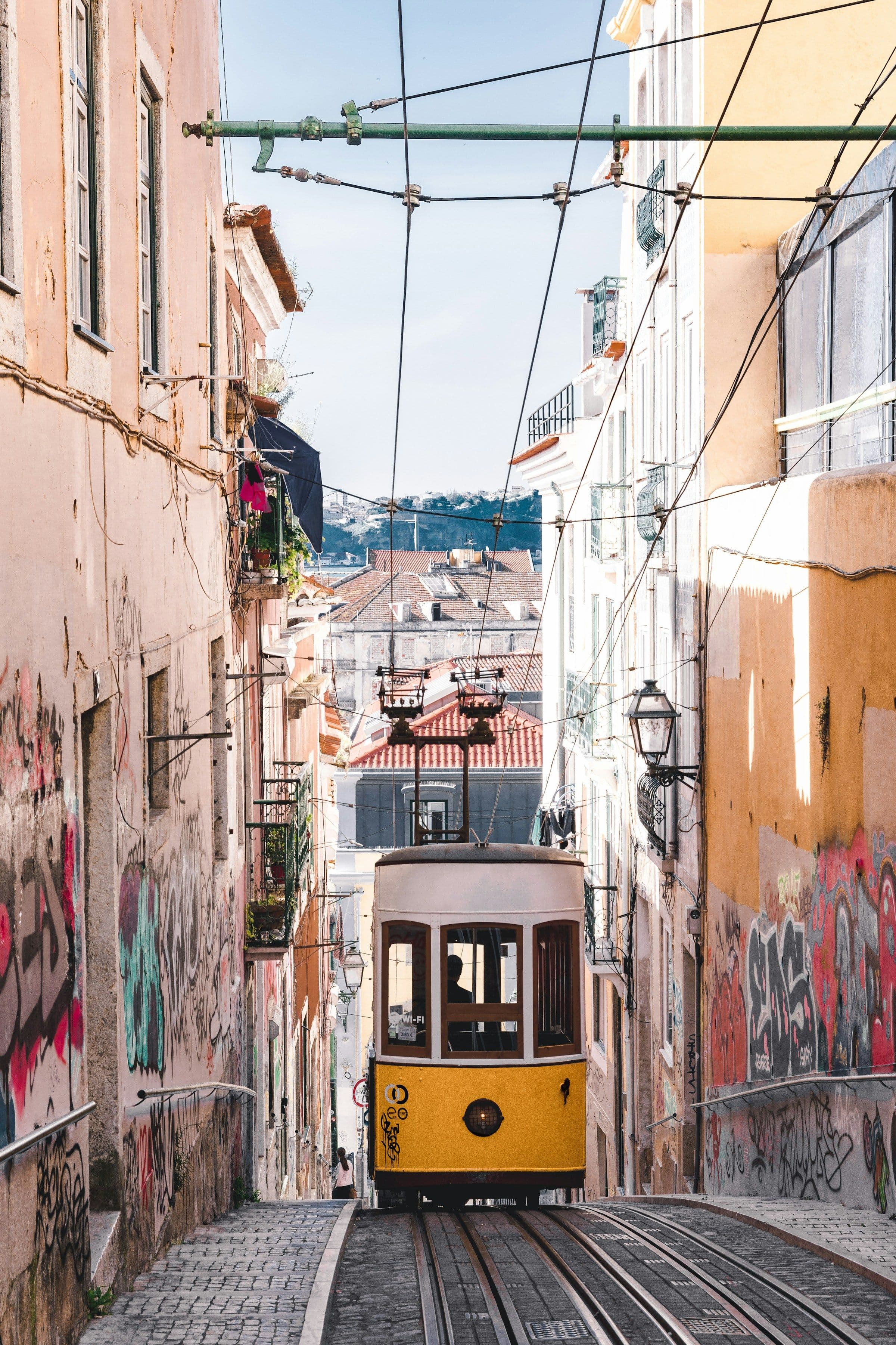 A yellow funicular tram climbing a narrow street in Lisbon, Portugal.