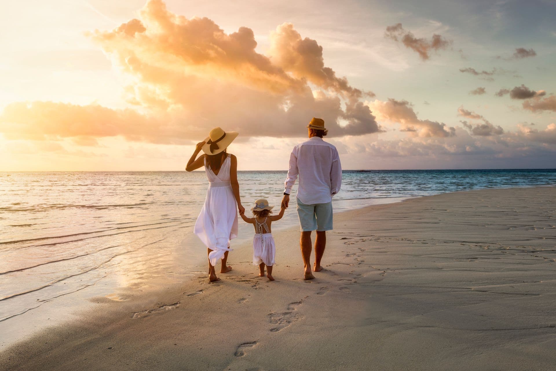 A mother and father walking hand in hand with their young daughter along a quiet beach at sunset.