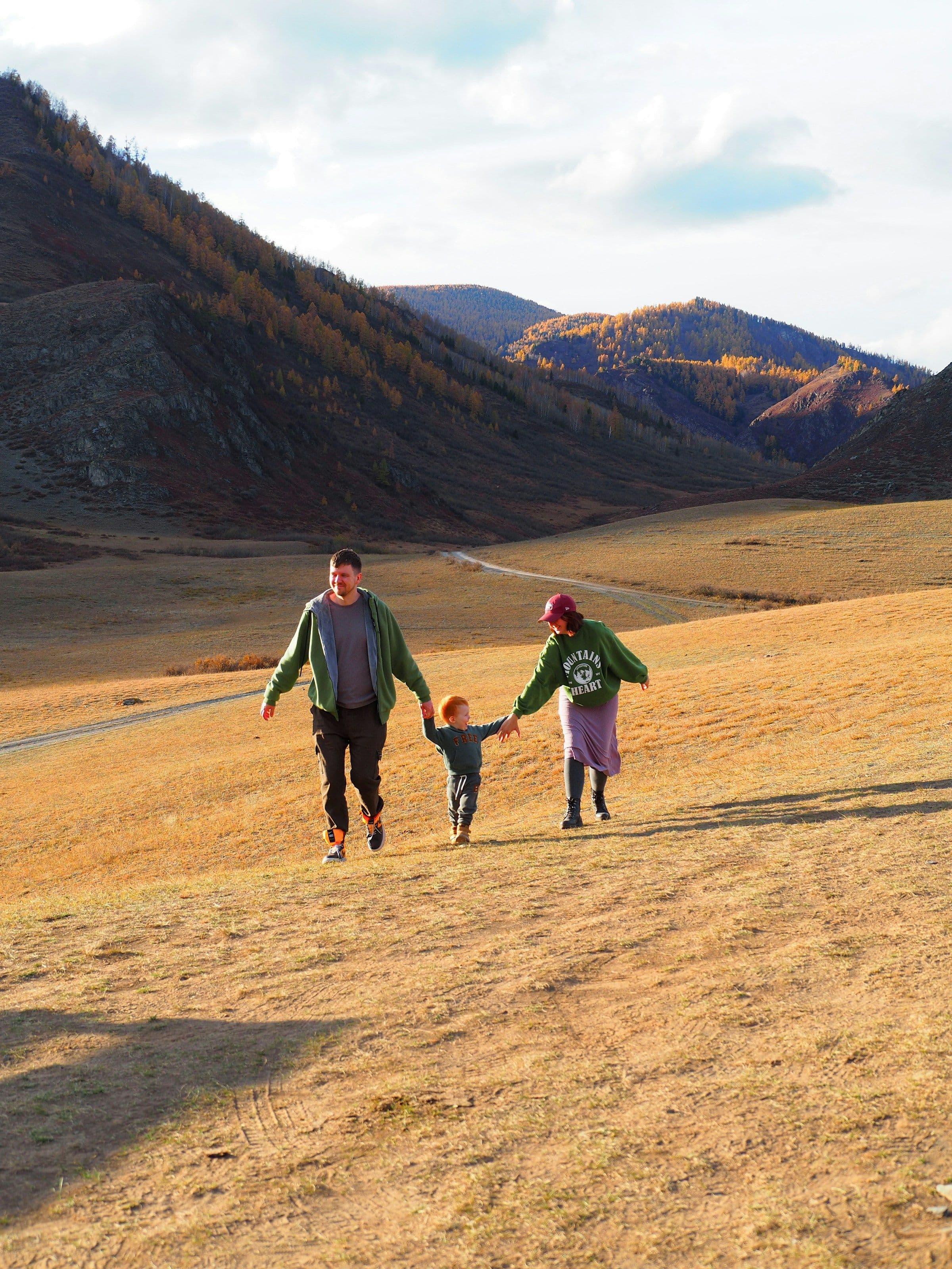 Two adults and a child holding hands as they run down a grassy hillside in the mountains.