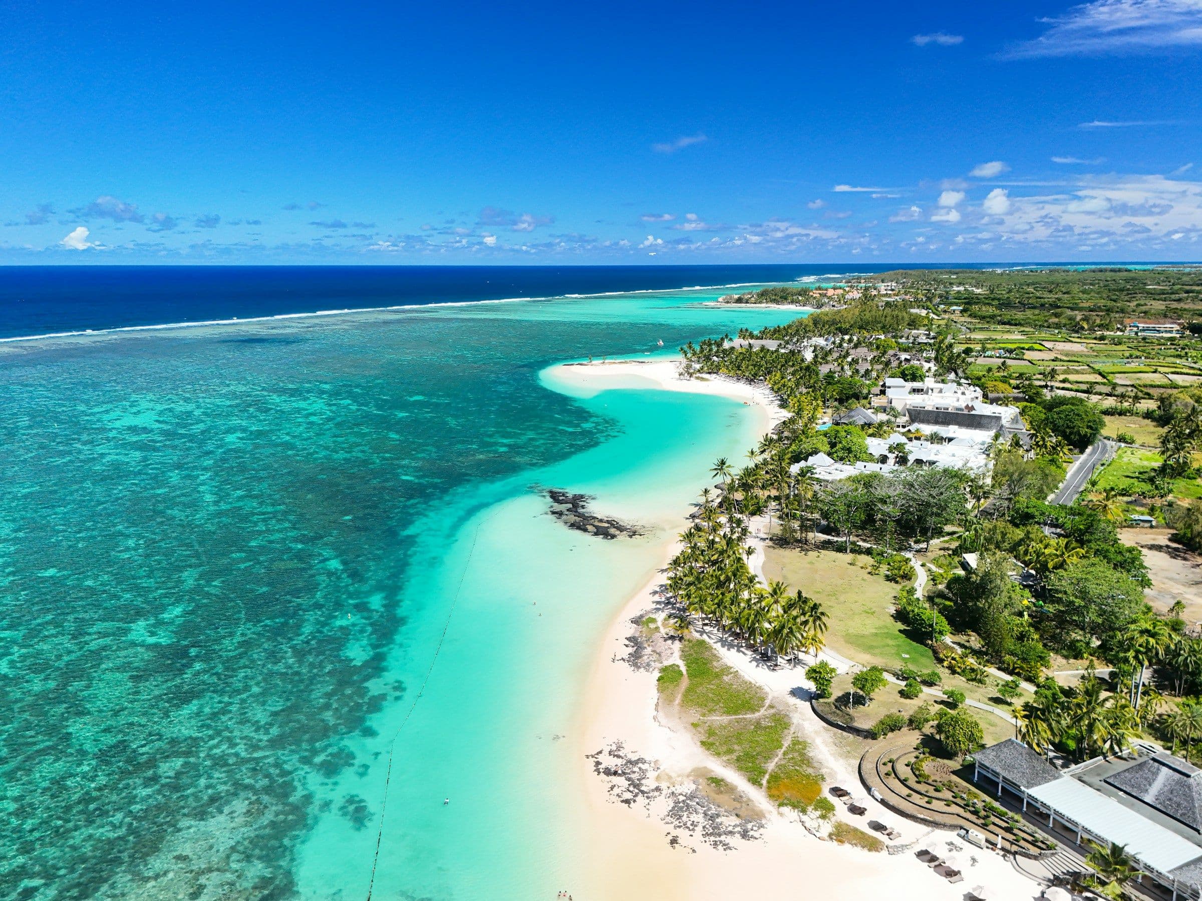 A long white beach, a wide turquoise lagoon and resort gardens at Belle Mare on the east coast of Mauritius, seen from the air.