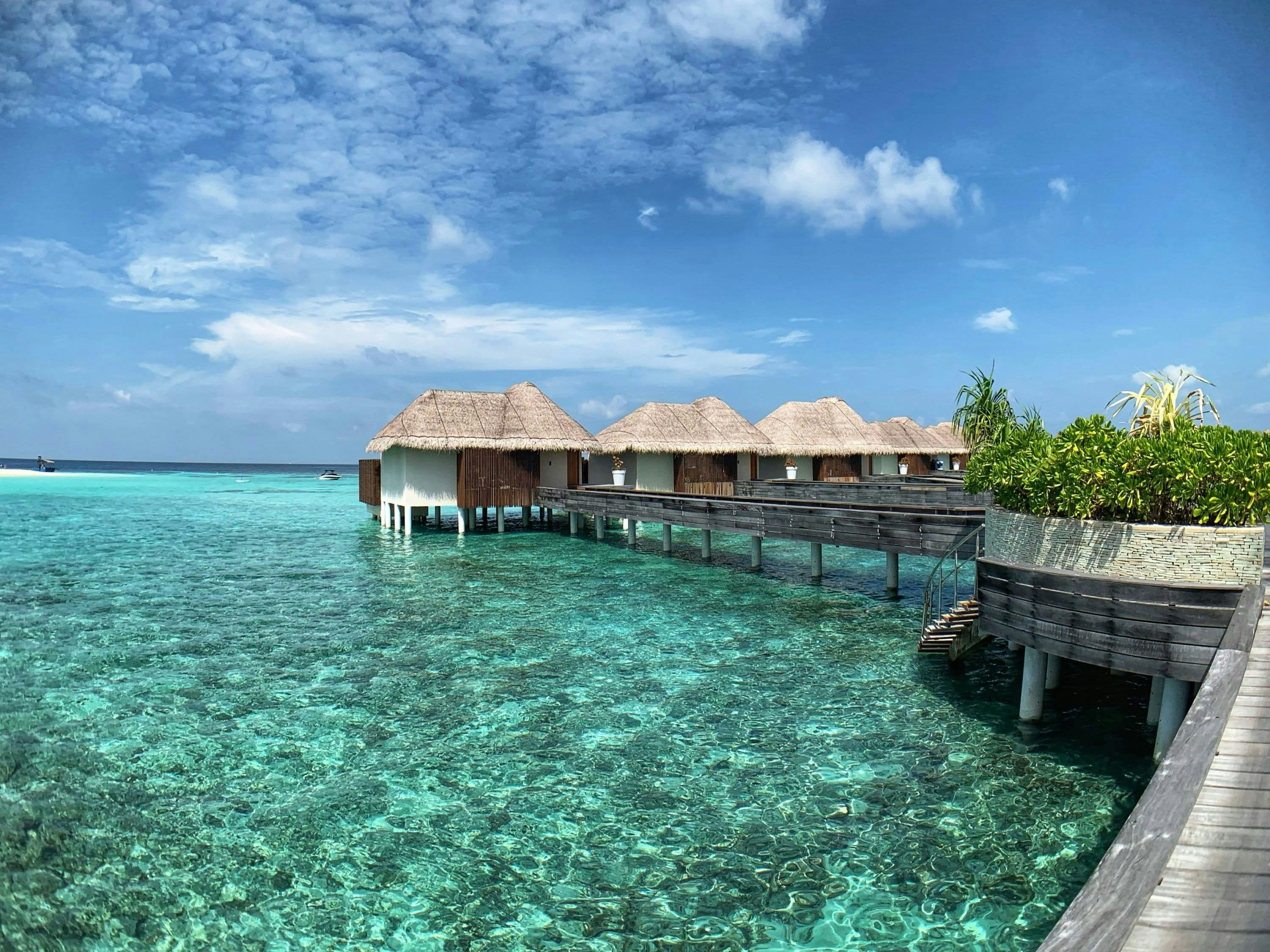 Thatched overwater villas on stilts above a clear turquoise lagoon in the Maldives.
