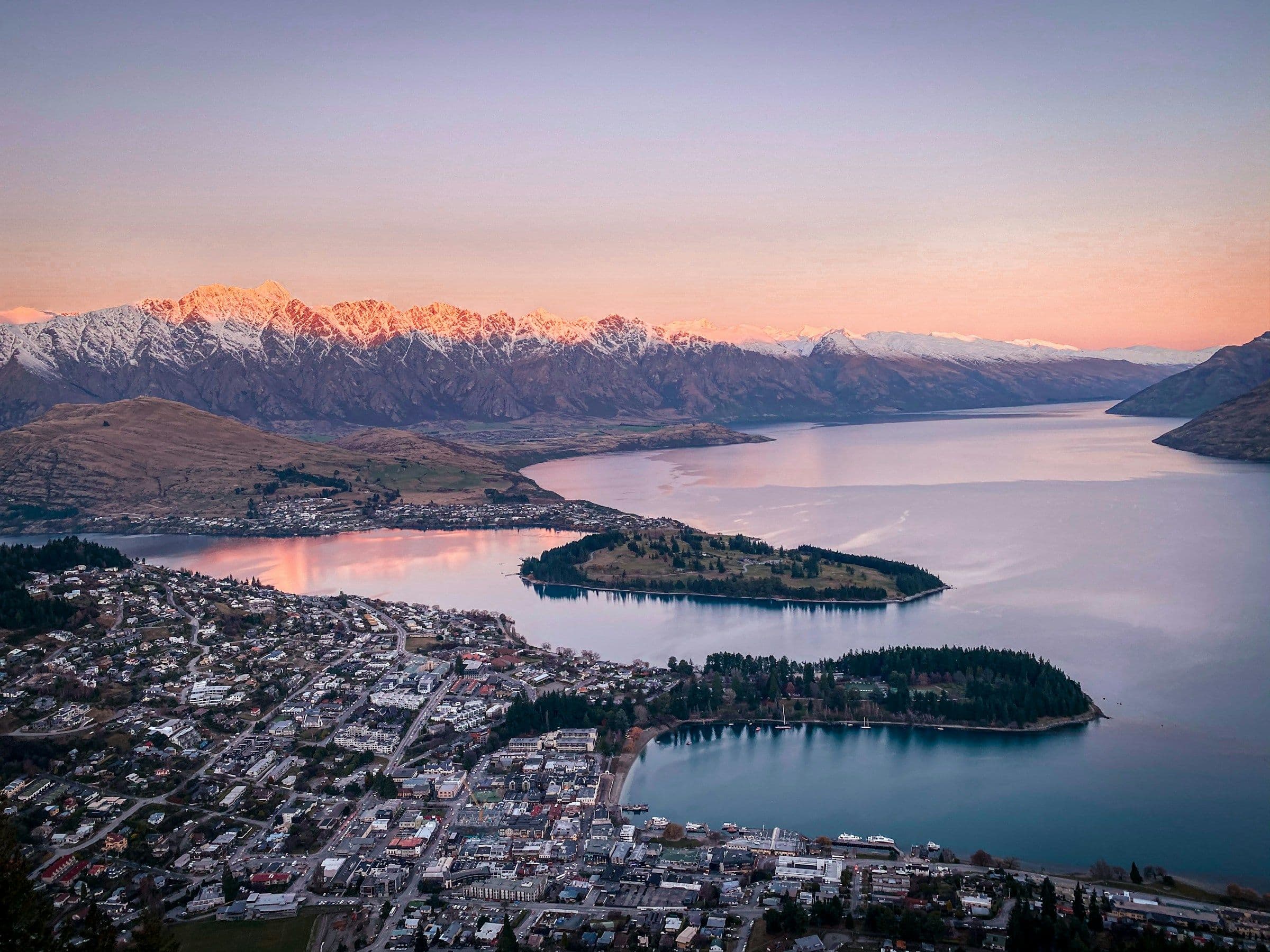 Queenstown on the shore of Lake Wakatipu, seen from above at dusk, with mountains behind.