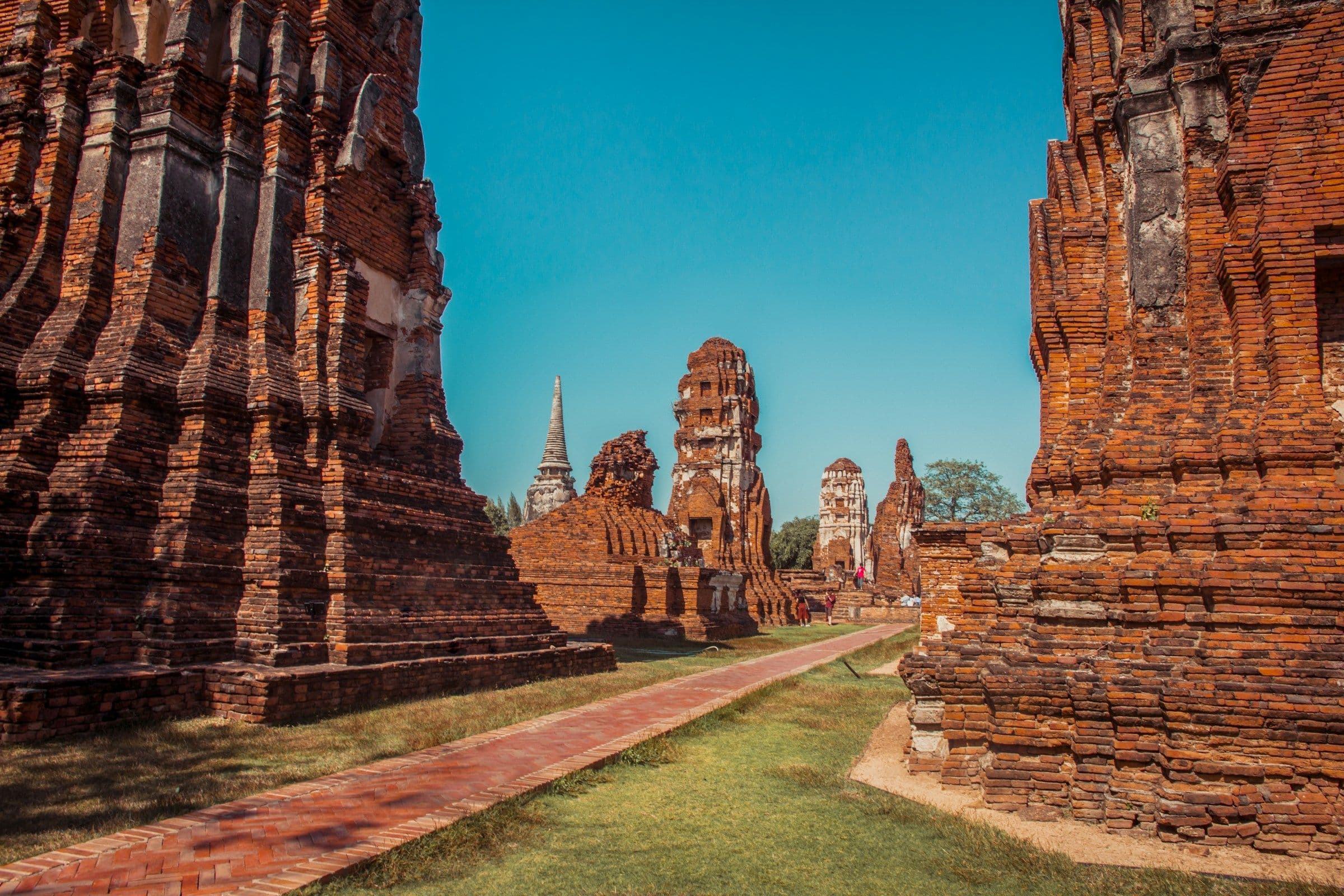 Brick towers and ruined temple walls beside a lawn at Ayutthaya, Thailand.