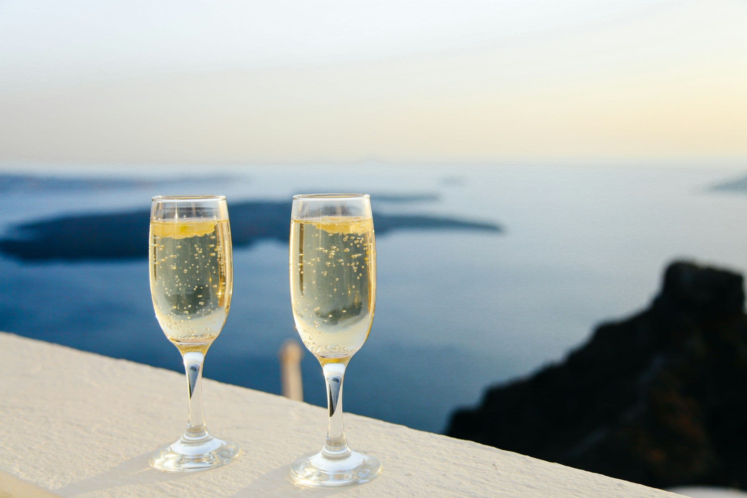 Two glasses of champagne on a white wall overlooking the sea in Santorini, Greece.