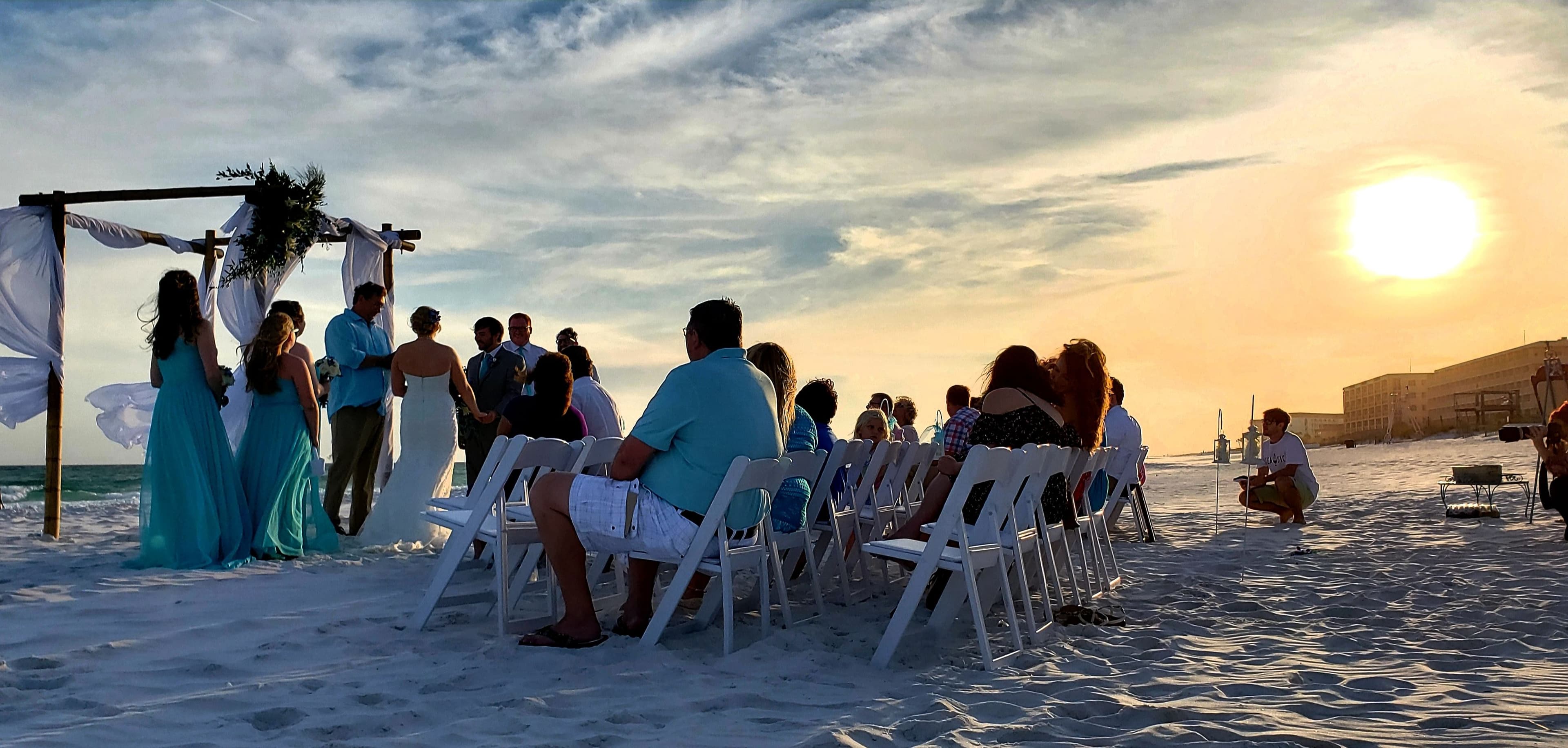 sunset beach wedding with guests and decorated arc