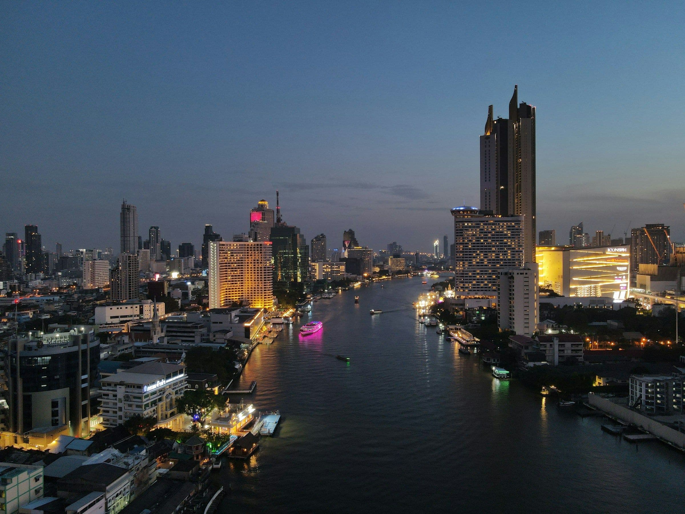The Chao Phraya river winding between the lit towers of Bangkok, Thailand, at dusk.
