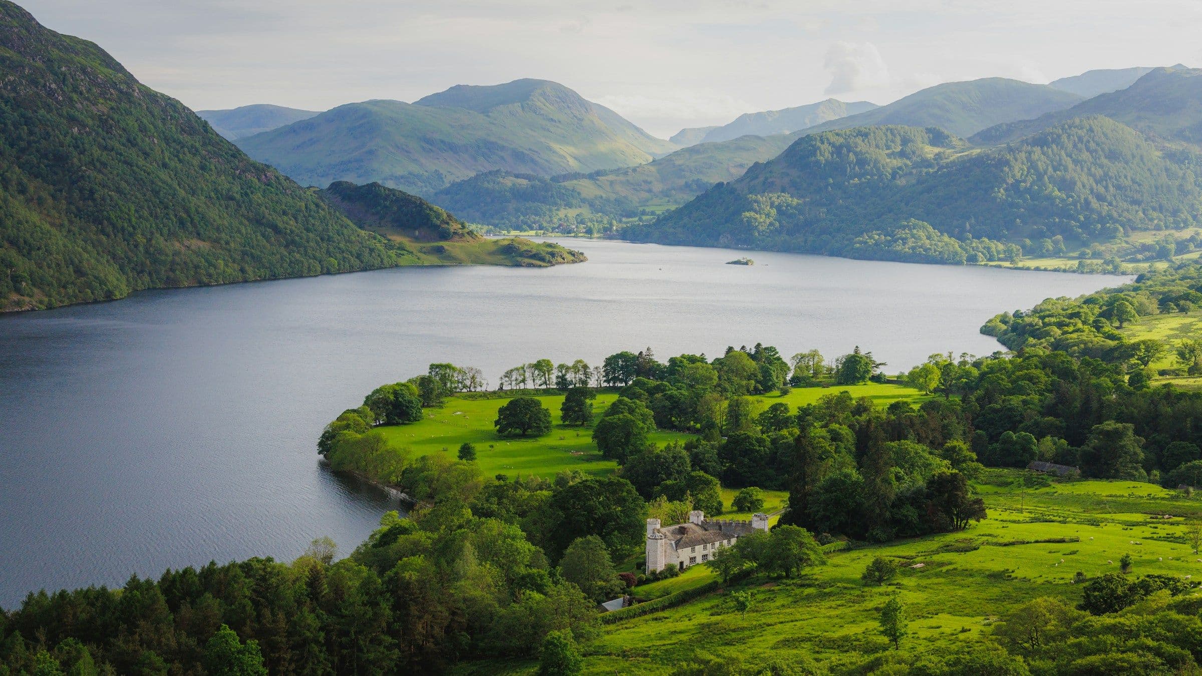 A lake surrounded by green fells and woodland in the Lake District.
