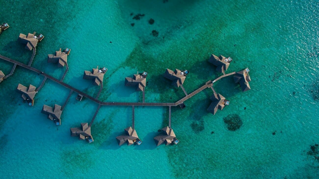 Overwater villas linked by a jetty over turquoise water.