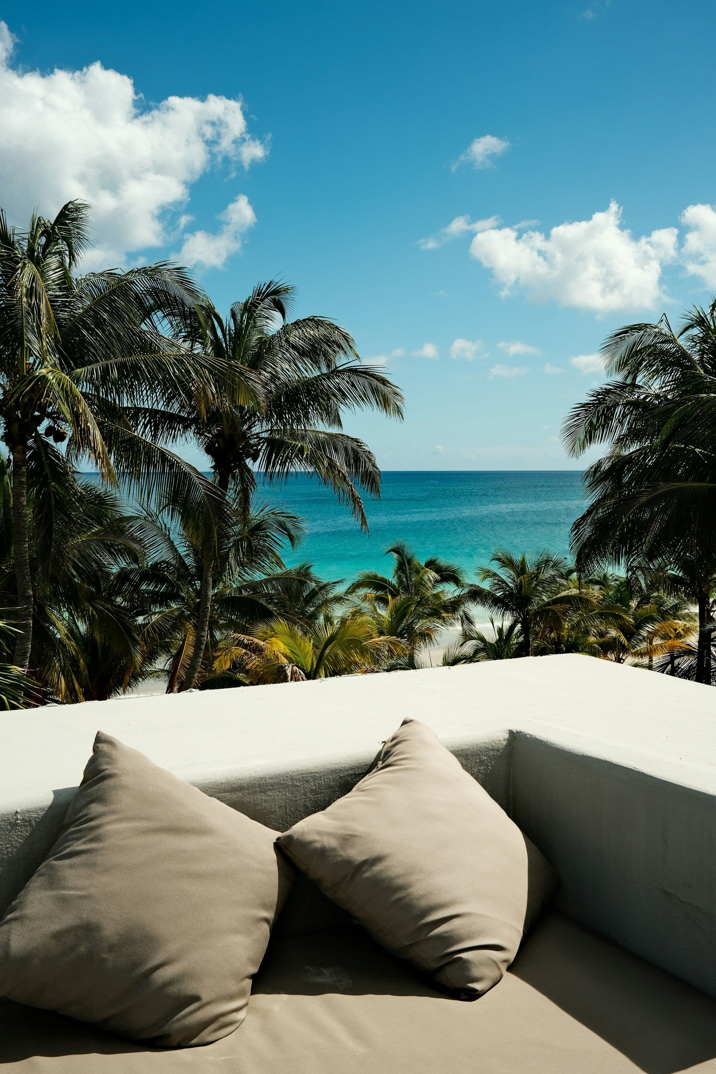 A cushioned outdoor sofa looking out over palm trees to a turquoise sea in Tulum, Mexico.