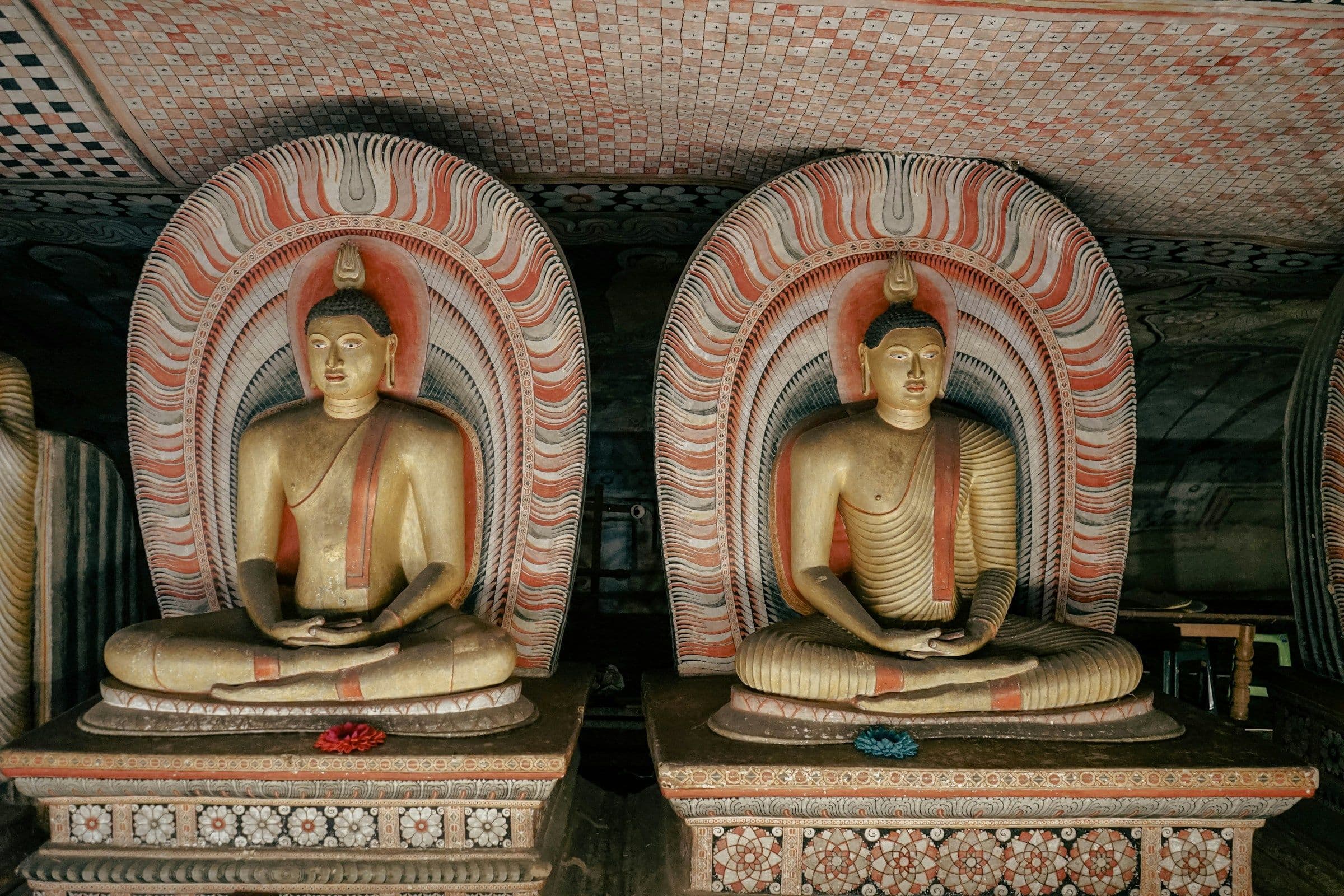 Two seated Buddha statues beneath painted arches in the Dambulla cave temple, Sri Lanka.