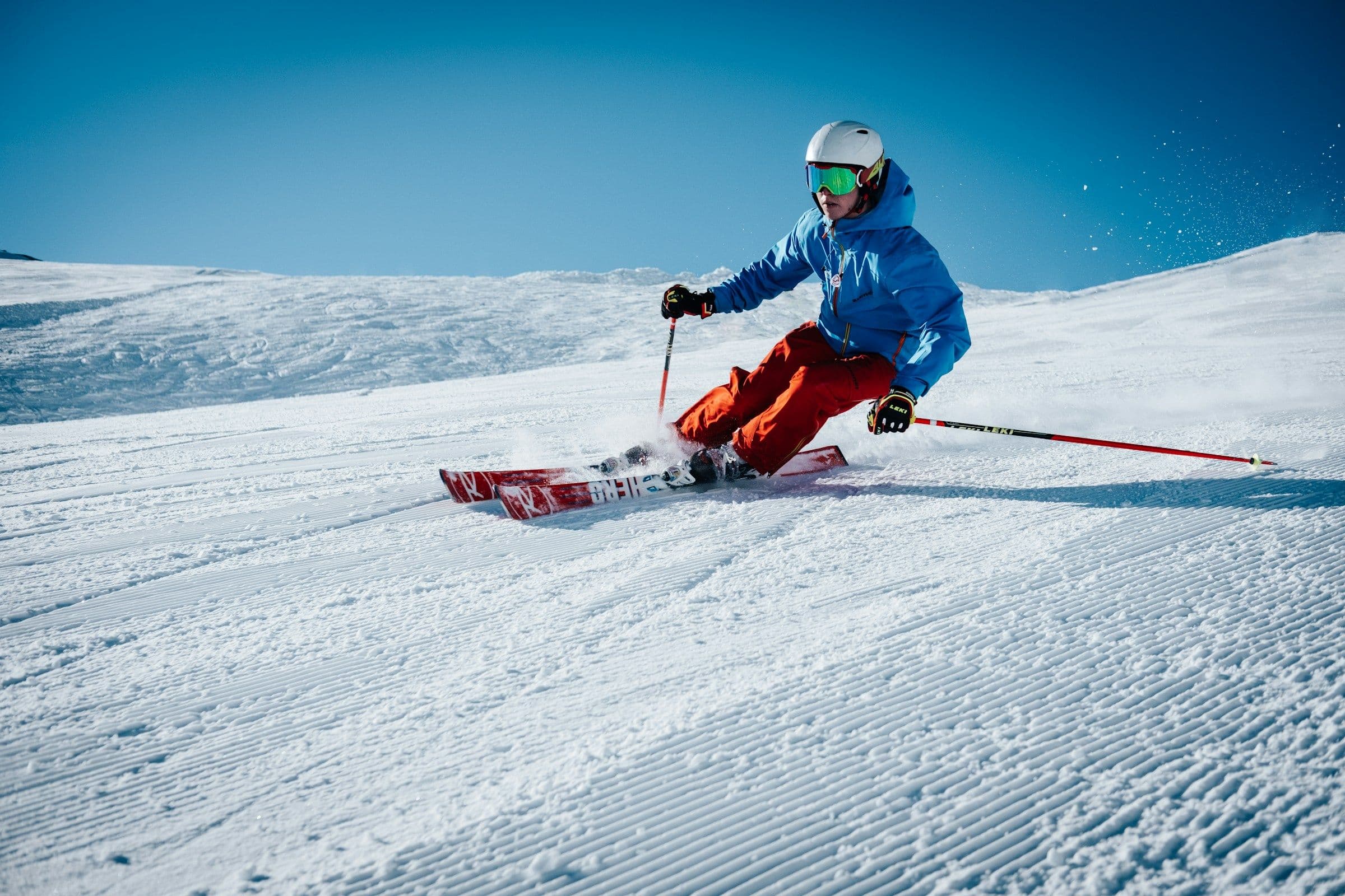 A skier in a blue jacket carving a turn on a freshly groomed piste in Austria.