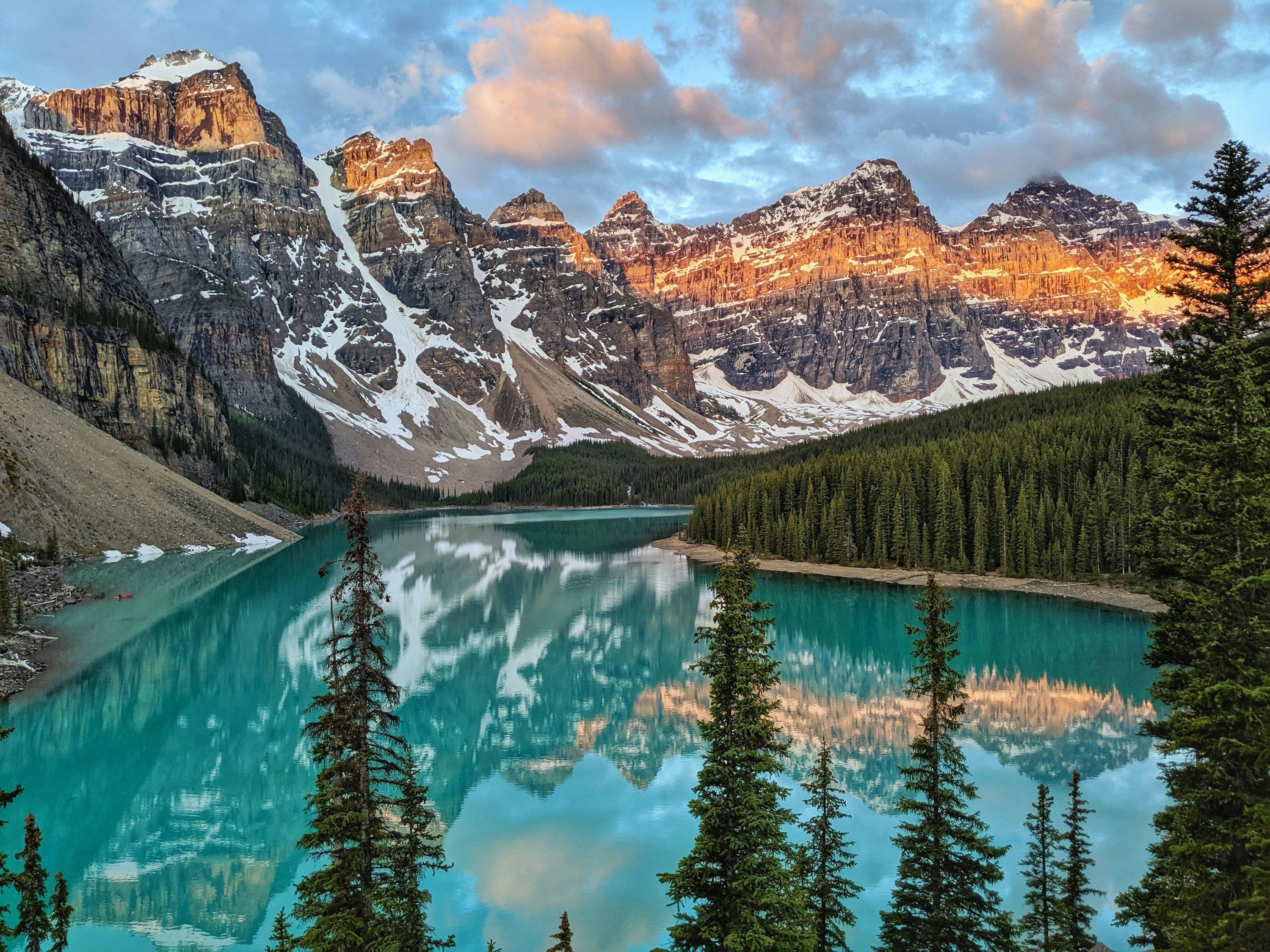 Moraine Lake in Banff National Park, Canada, its turquoise water ringed by pine trees and peaks lit by the early sun.