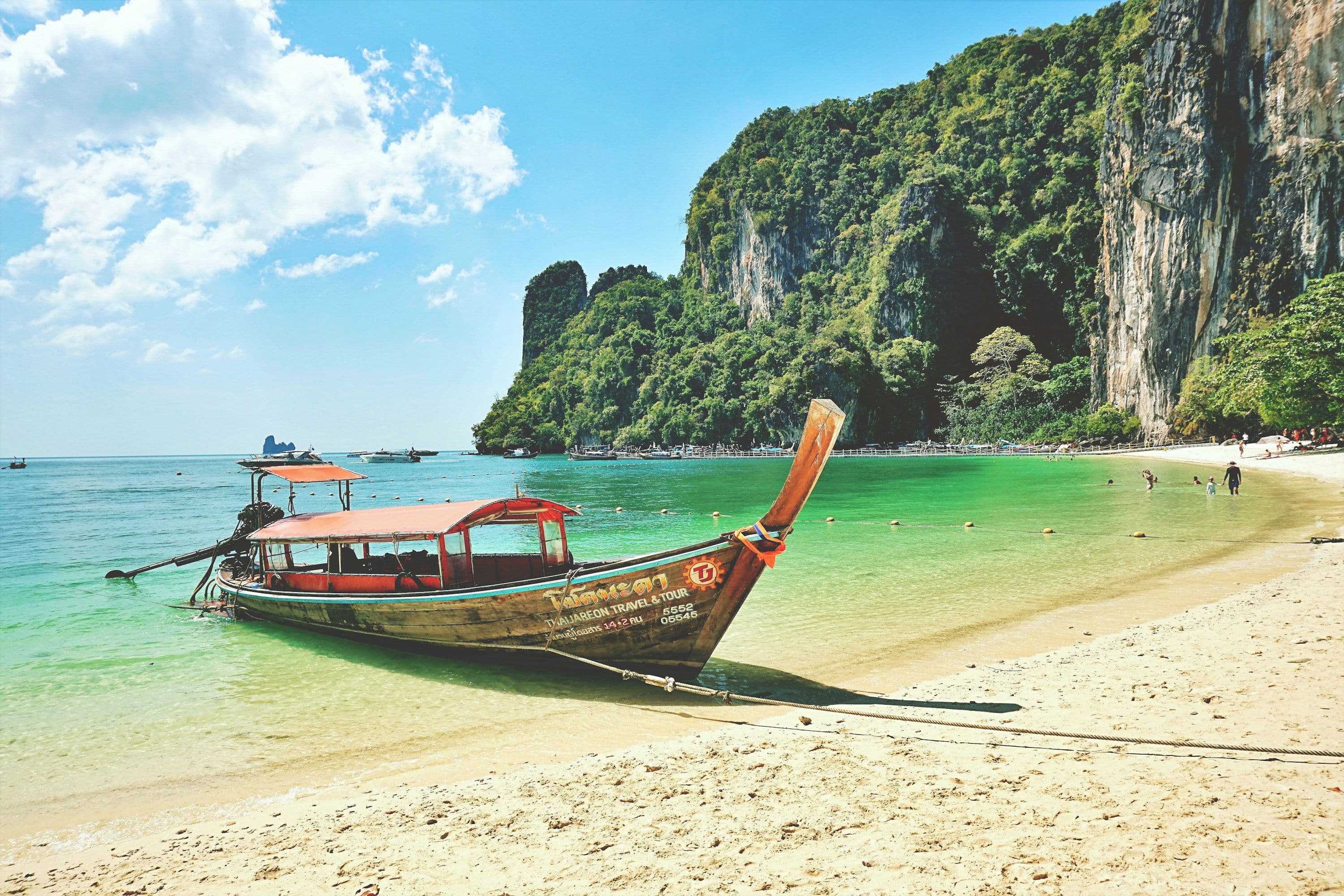 A traditional longtail boat drawn up on a sandy beach beneath limestone cliffs at Ko Hong, Thailand.